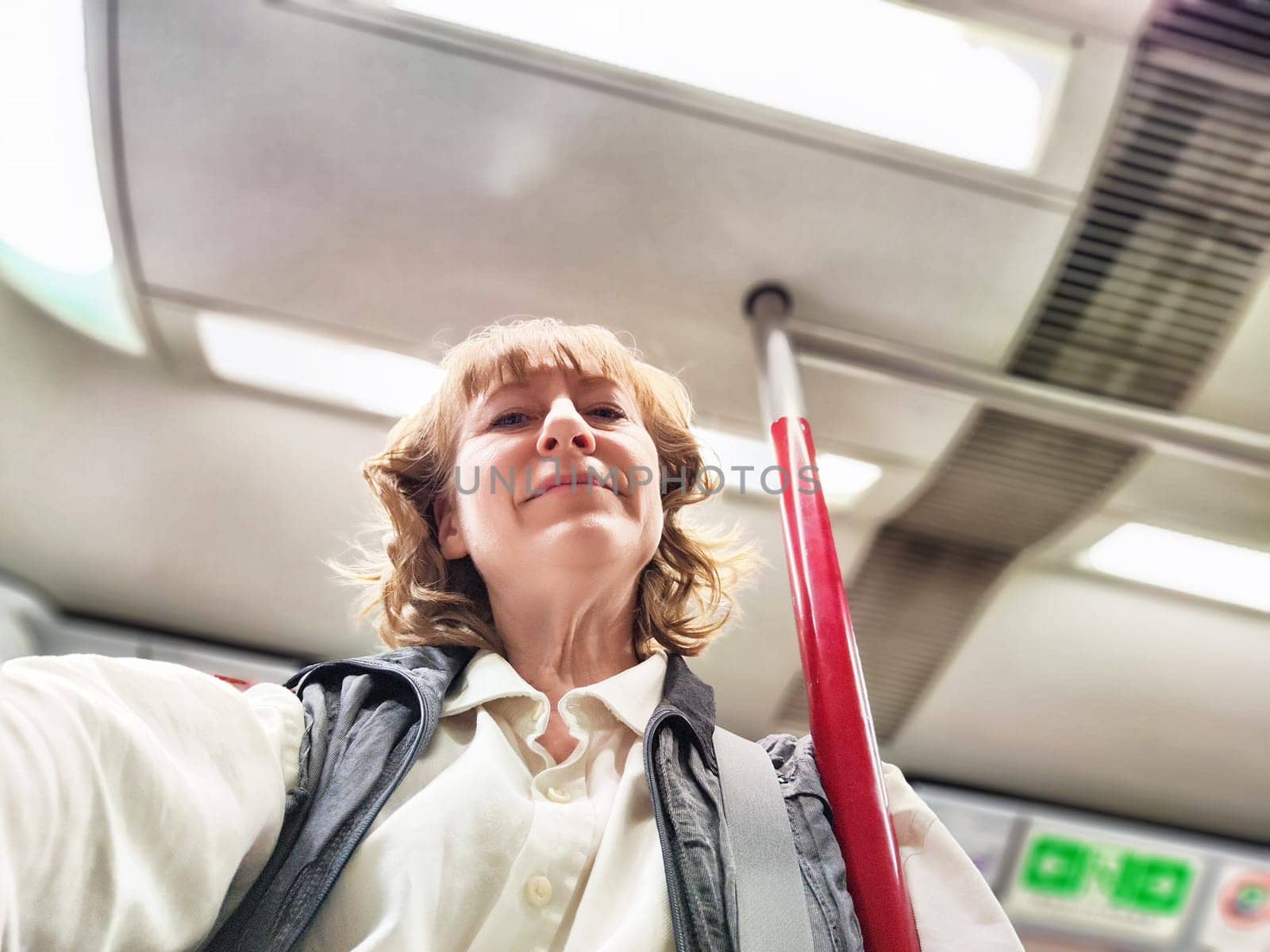 A middle-aged woman takes a selfie while holding onto a pole in a subway train, experiencing urban travel and adventure.