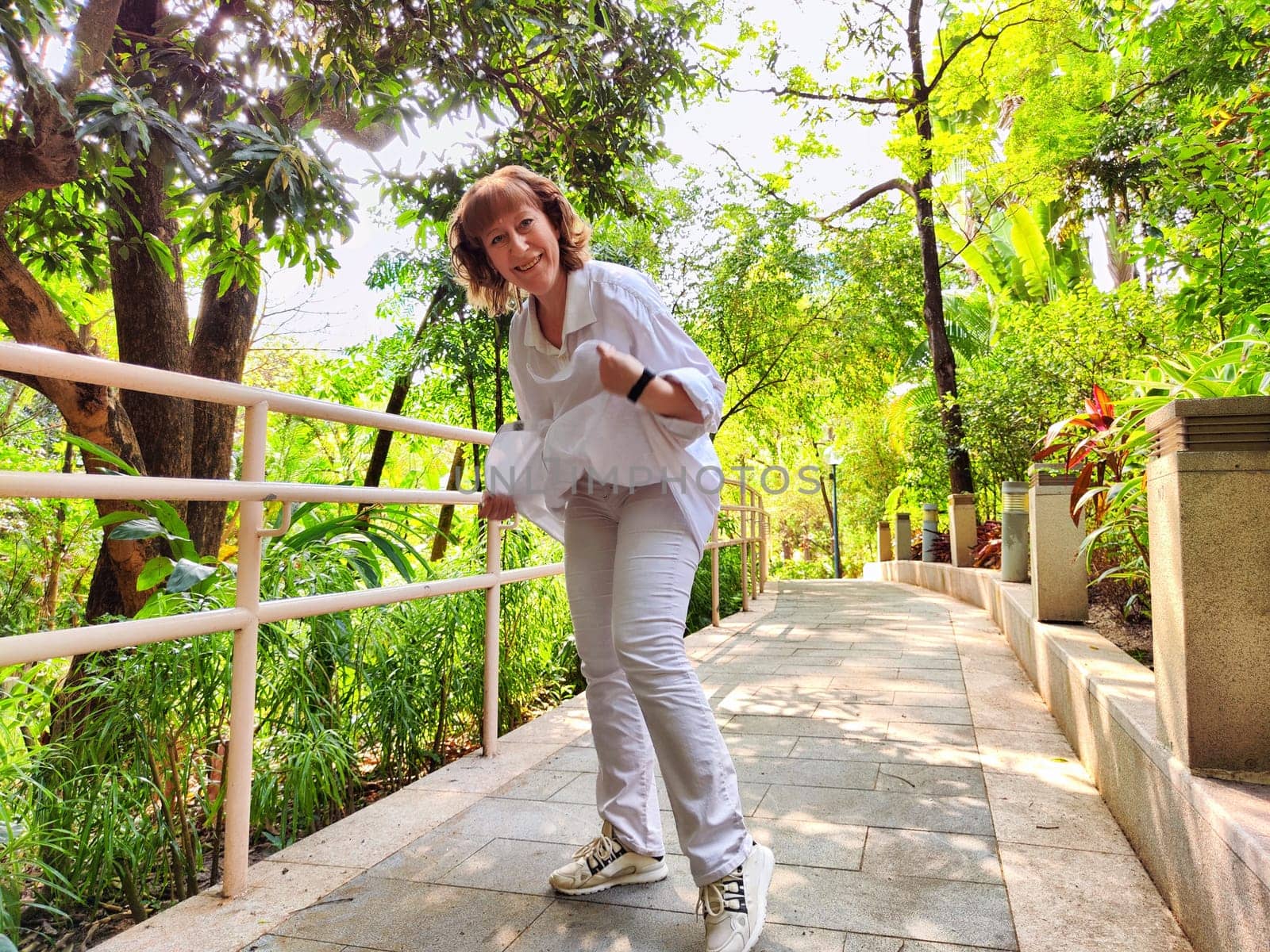 Blonde woman captures a joyful moment while exploring a lush green area, surrounded by vibrant plants and trees.