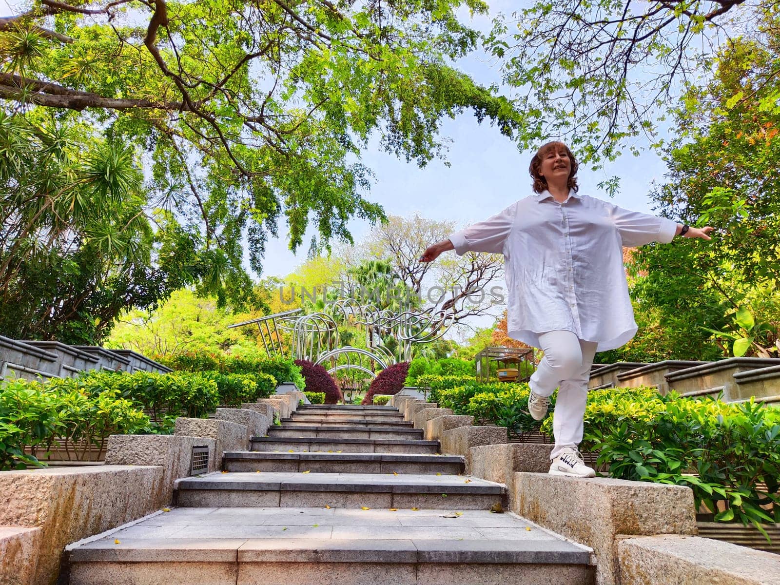 Blonde woman smiles joyfully as she poses on steps in a beautiful outdoor setting during a travel excursion.