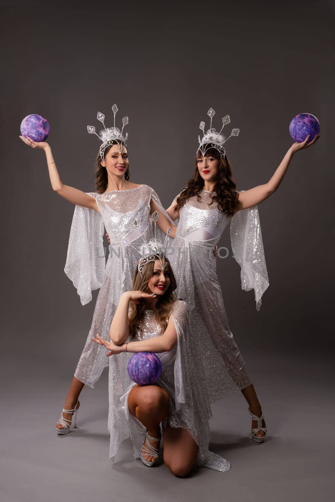 Full body of young bride in white dress and veil holding blue balloon in hands and looking at camera against gray background
