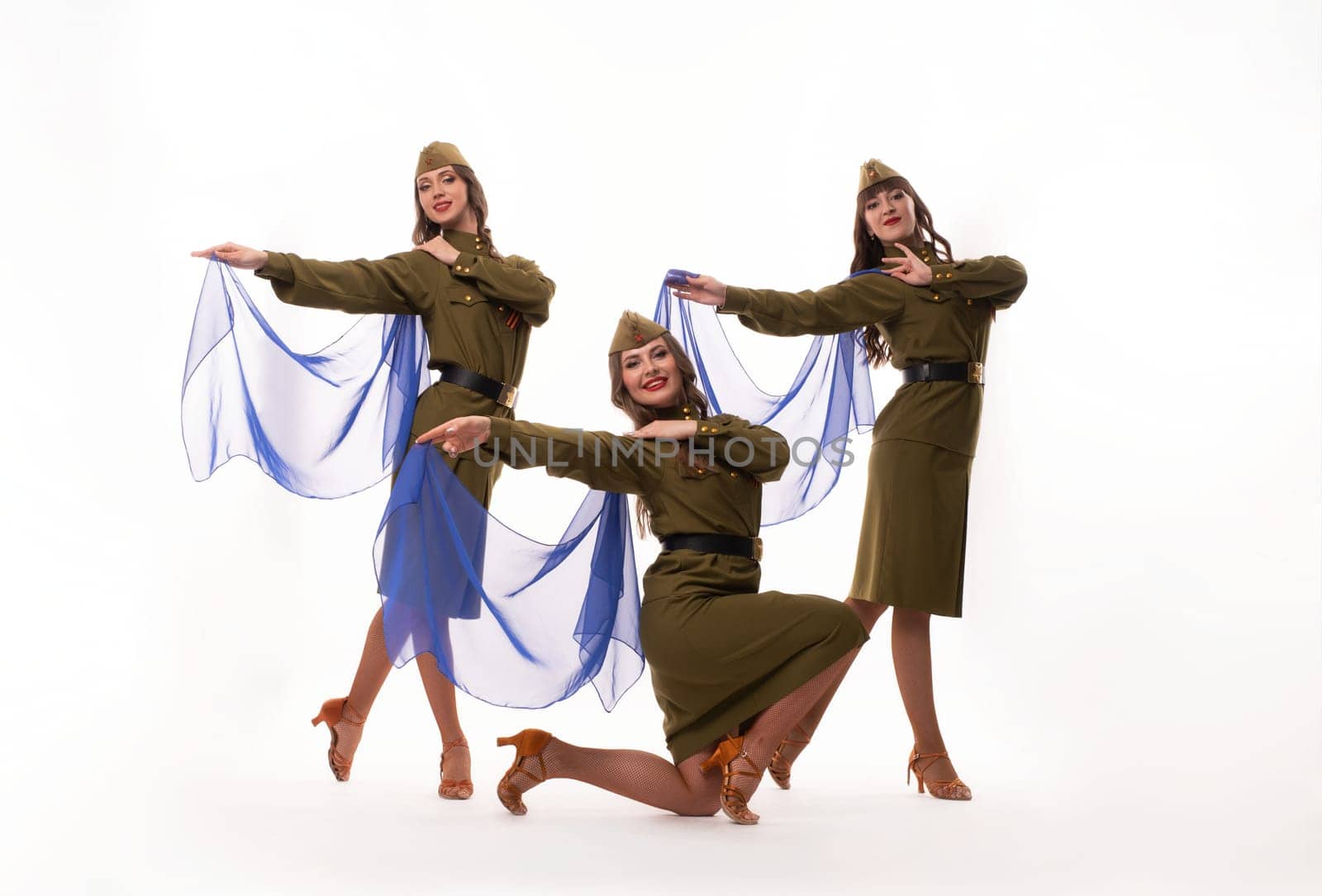 Full body of happy young female friends in trendy outfits smiling and looking at camera while dancing against white background