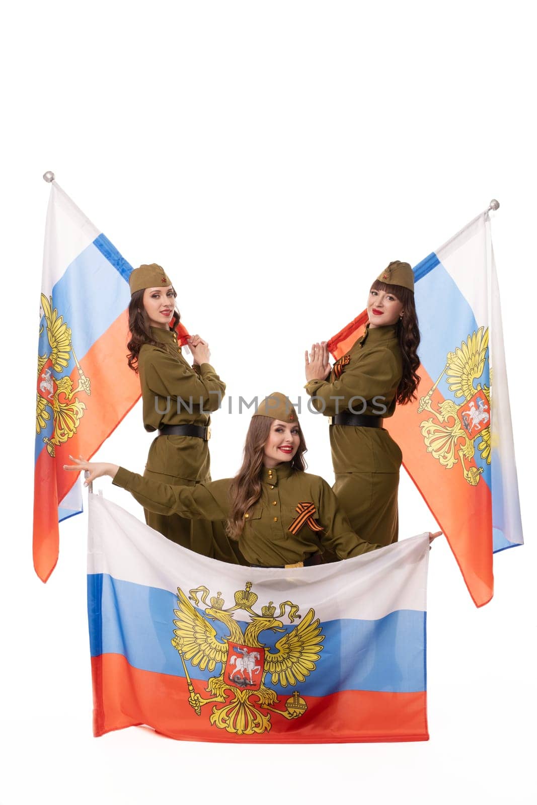 Delighted female models in military clothes with St George ribbons holding Russian flags and looking at camera against white background