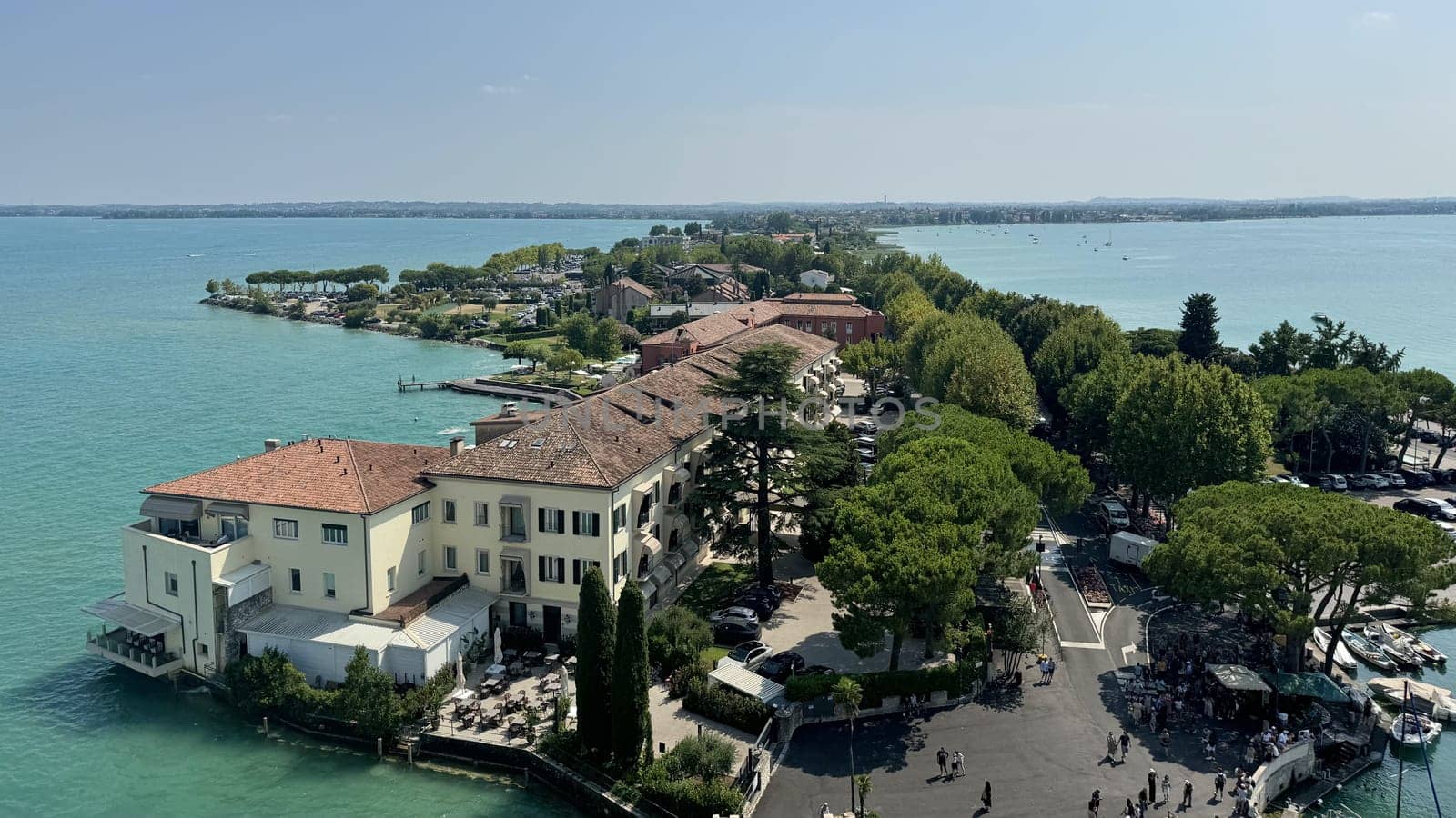 Unique Sirmione Peninsula Encircled by the Crystal Waters of Lake Garda, Italy. A breathtaking view of the Sirmione peninsula, dramatically surrounded by the clear, sparkling waters of Lake Garda. This iconic Italian destination combines historic charm with natural beauty, featuring medieval buildings, lush greenery, and serene lake vistas on both sides. A must-visit location for travelers seeking captivating scenery and cultural richness.