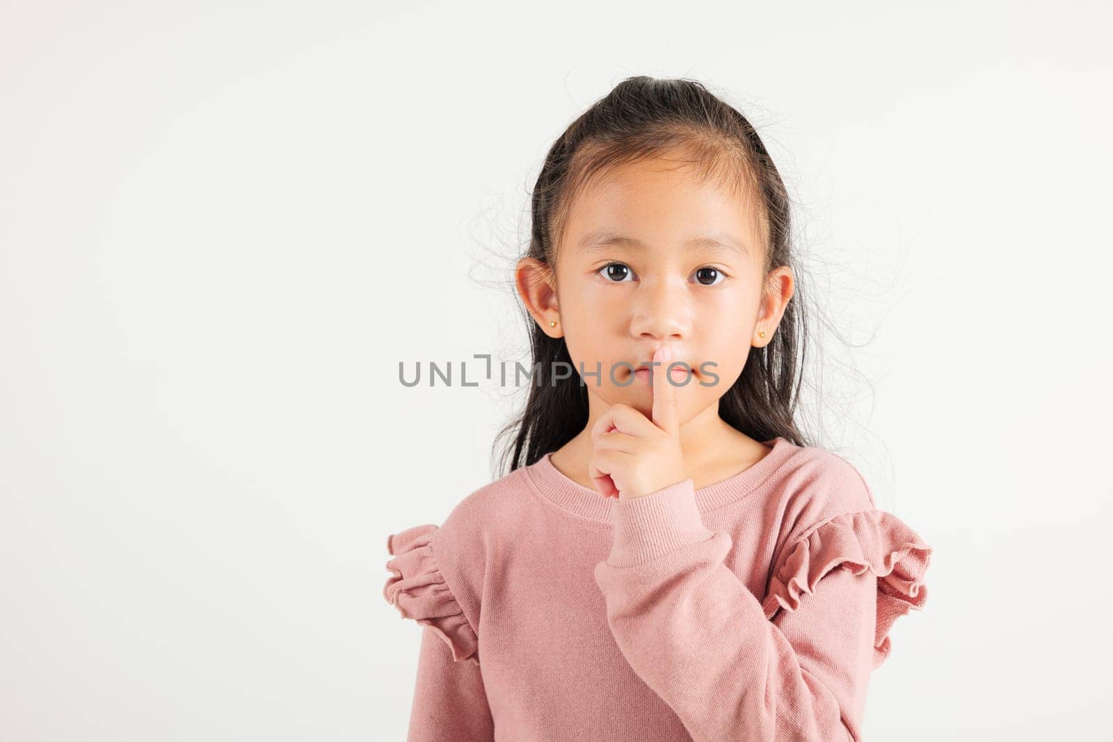 Young kid girl making finger on lips mouth silent quiet gesture, Happy Asian kindergarten child marking silence for stop quiet, mute studio shot isolated on white background with copy space