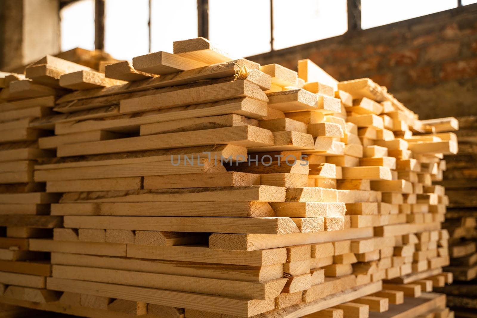 Stack of wooden planks captured indoors in golden sunlight, showing warm color tones, soft shadows, and orderly arrangement of timber used in woodworking or construction.