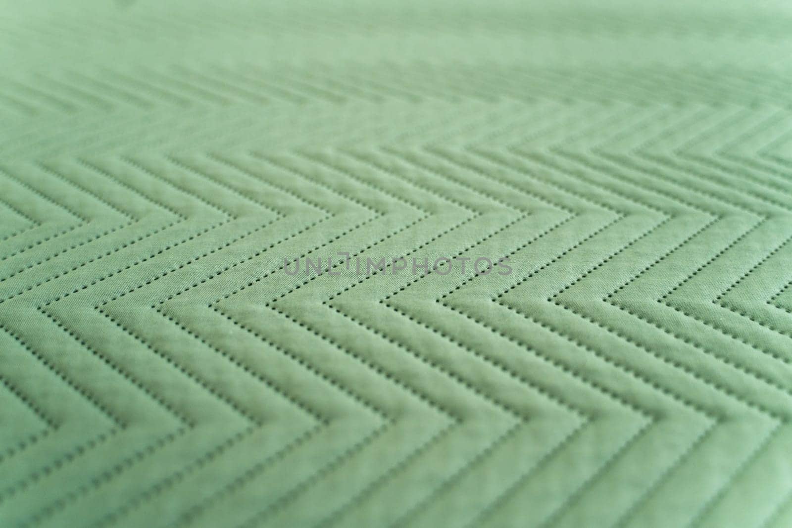 Textile surface in green color featuring regular zigzag stitching and punctured details forming a geometric fabric pattern, ideal for design, sewing, or textile concepts.