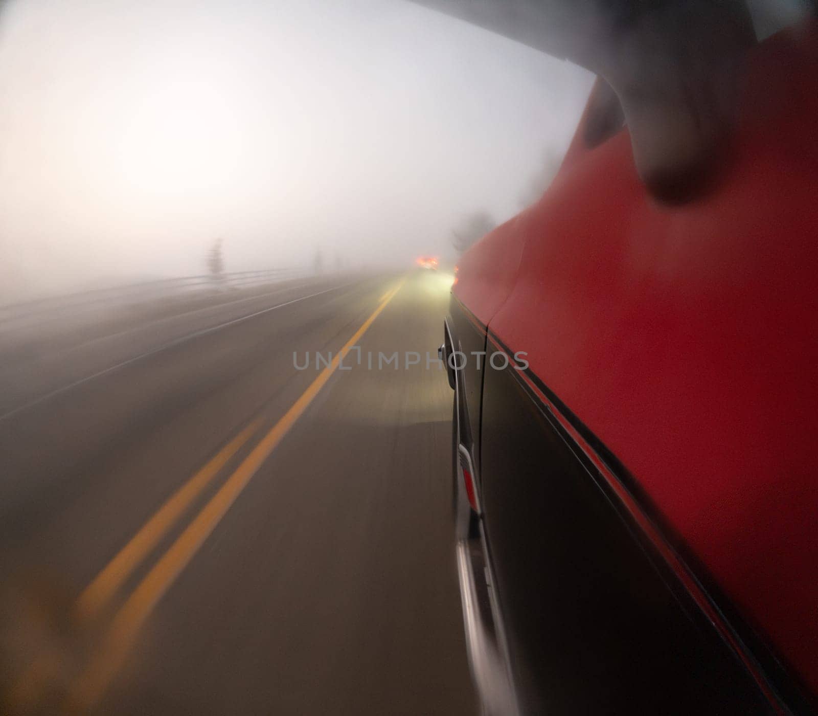 A blurry shot of a car driving down a foggy road. The car is red and the road is yellow
