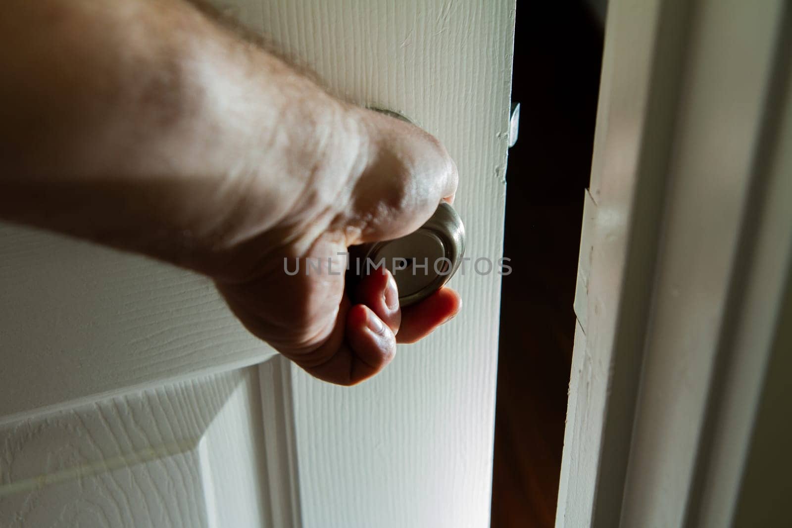 A hand is holding a door open. The door is white and the hand is visible. Scene is casual and relaxed
