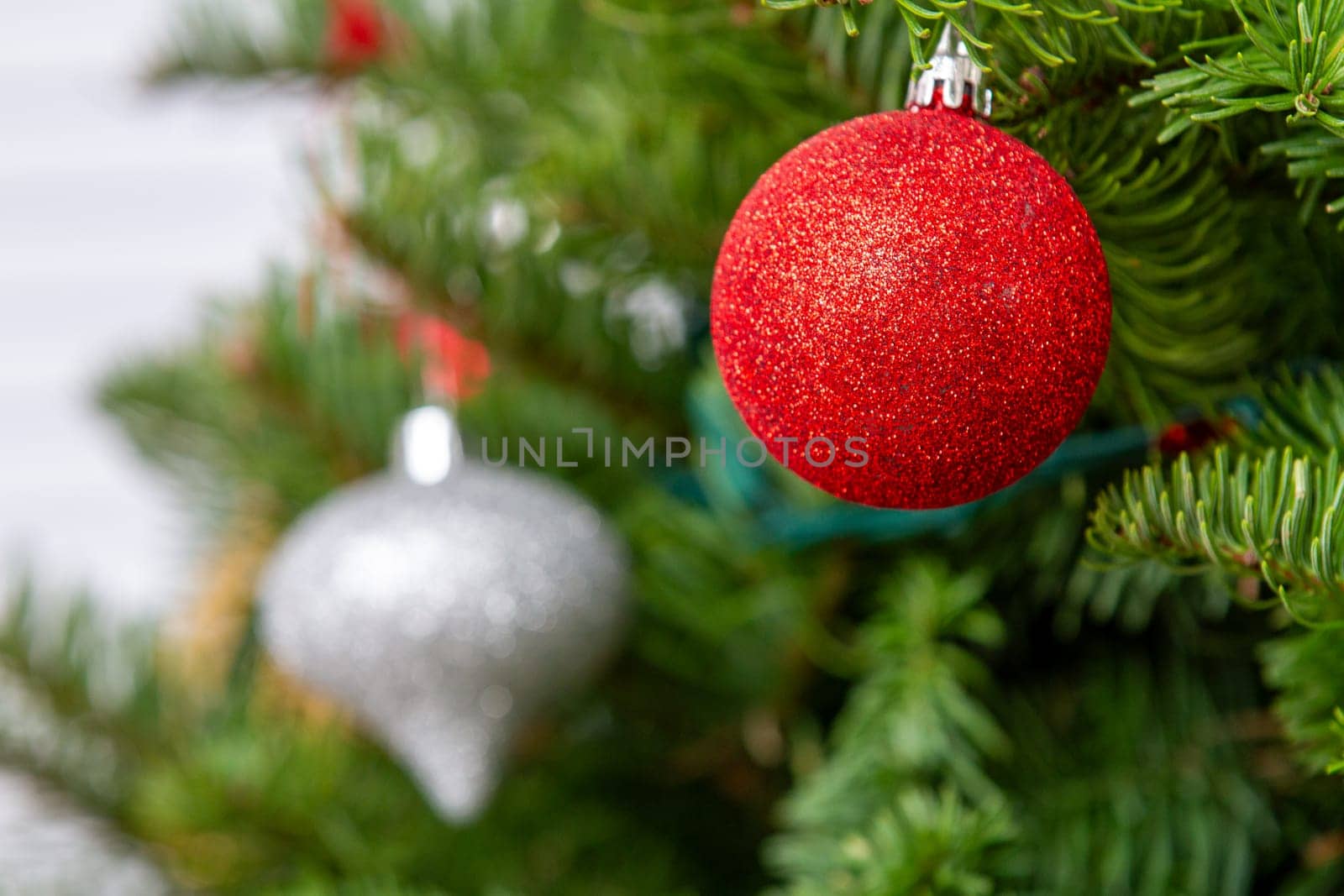 A red and silver ornament hangs on a Christmas tree. The tree is full of green leaves, and the ornaments are hanging from the branches
