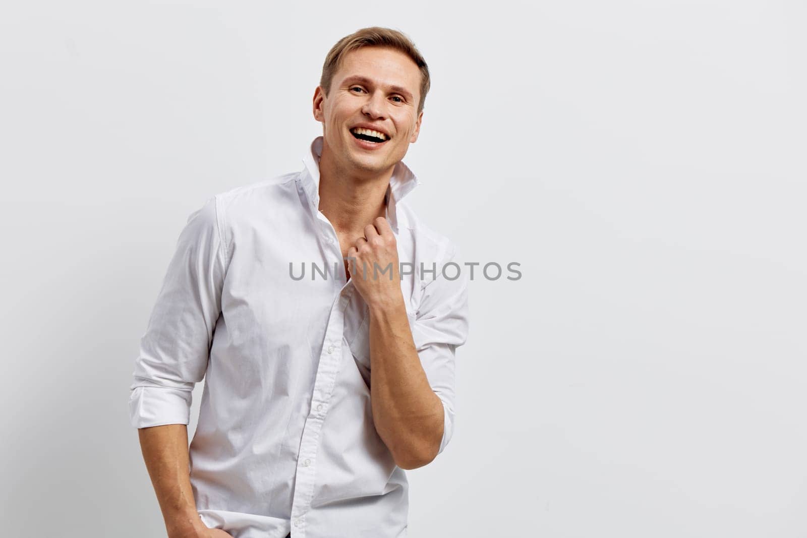 Happy smiling man in white shirt with rolled-up sleeves looking joyful against a plain gray background. Confident and relaxed expression, casual attire, middle-aged male model, positive energy, studio shot, lifestyle concept.