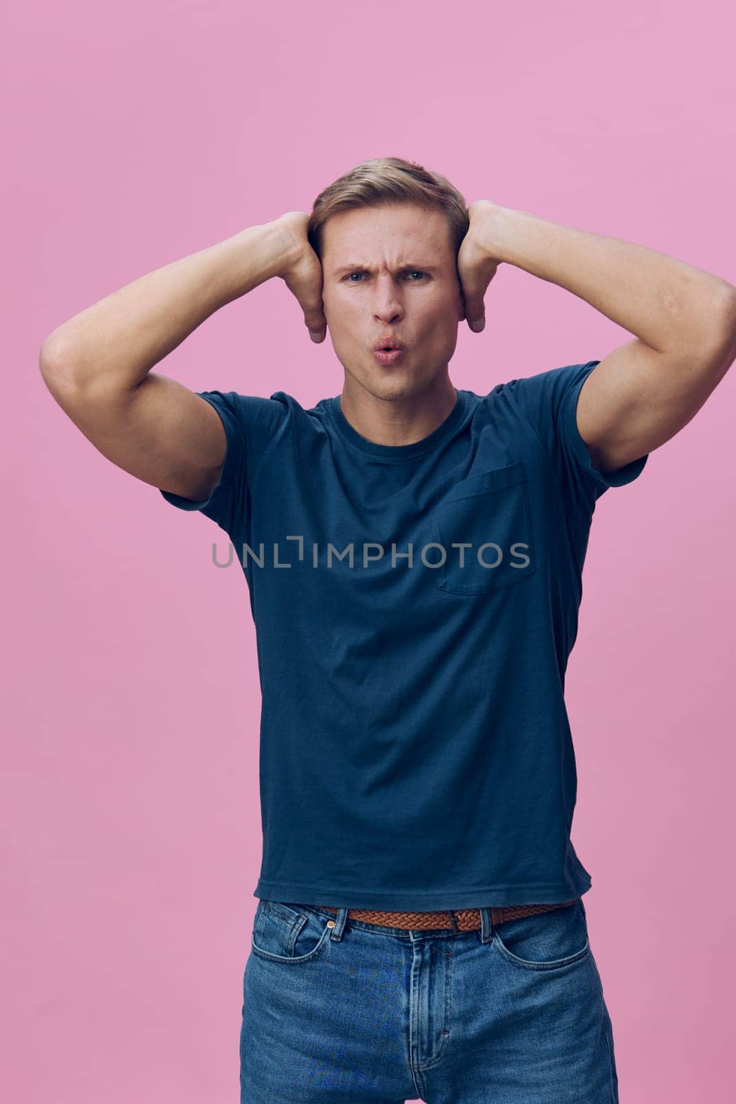 frustrated man wearing blue t-shirt hold head with both hands show annoyed and stressed expression with pink background representing mental health and gadgets interaction concept