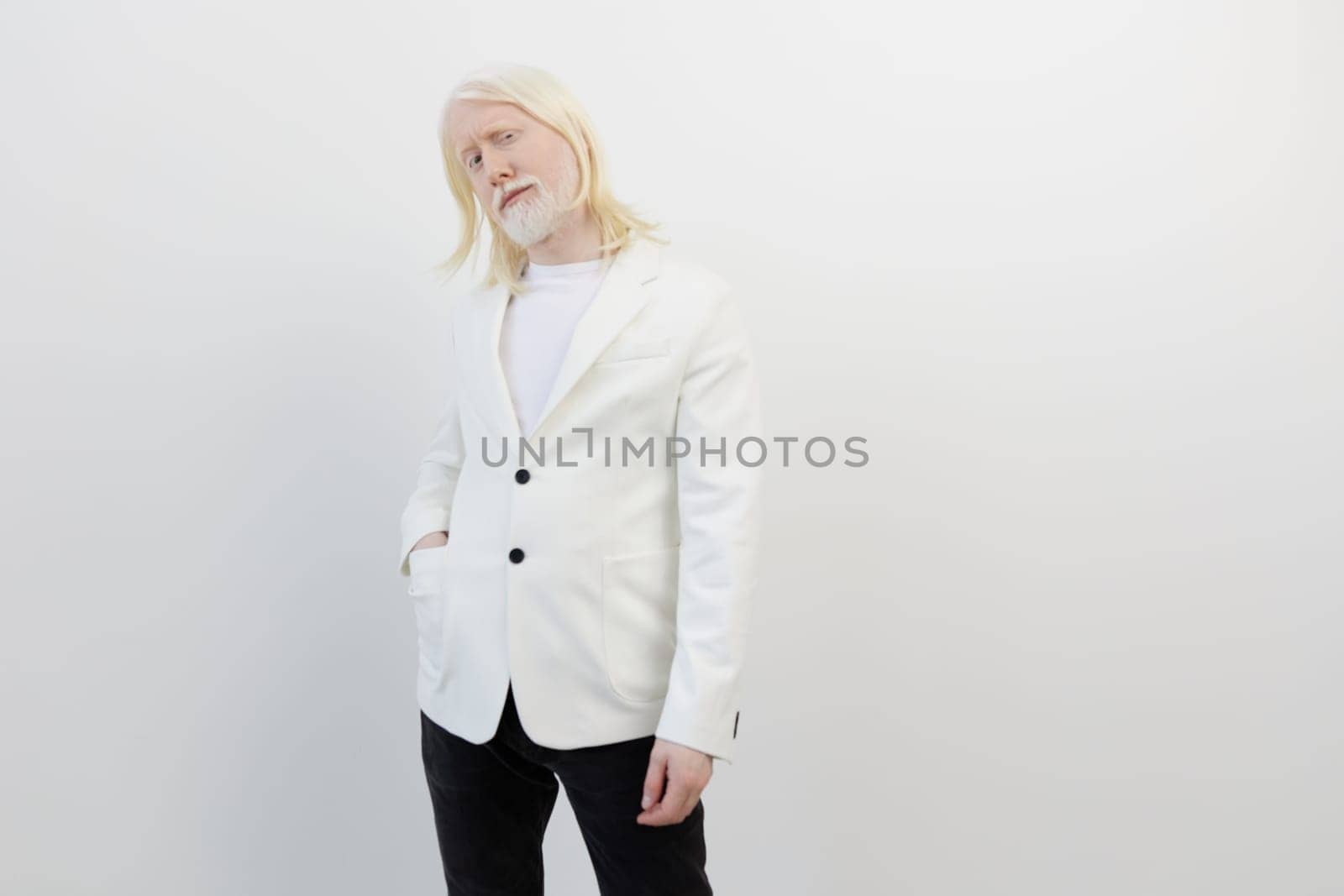 This image features a fashionable man in a white blazer and black trousers, presenting a unique pose against a clean, white background The minimalist setting emphasizes his stylish appearance and contemporary vibe