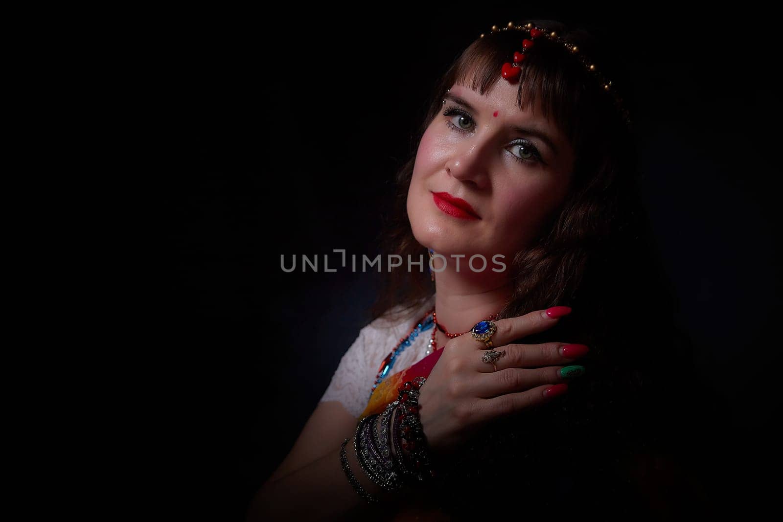 A middle-aged woman showcases her stunning sari while posing gracefully, highlighting her jewelry and vibrant makeup in an Indian-themed shoot.
