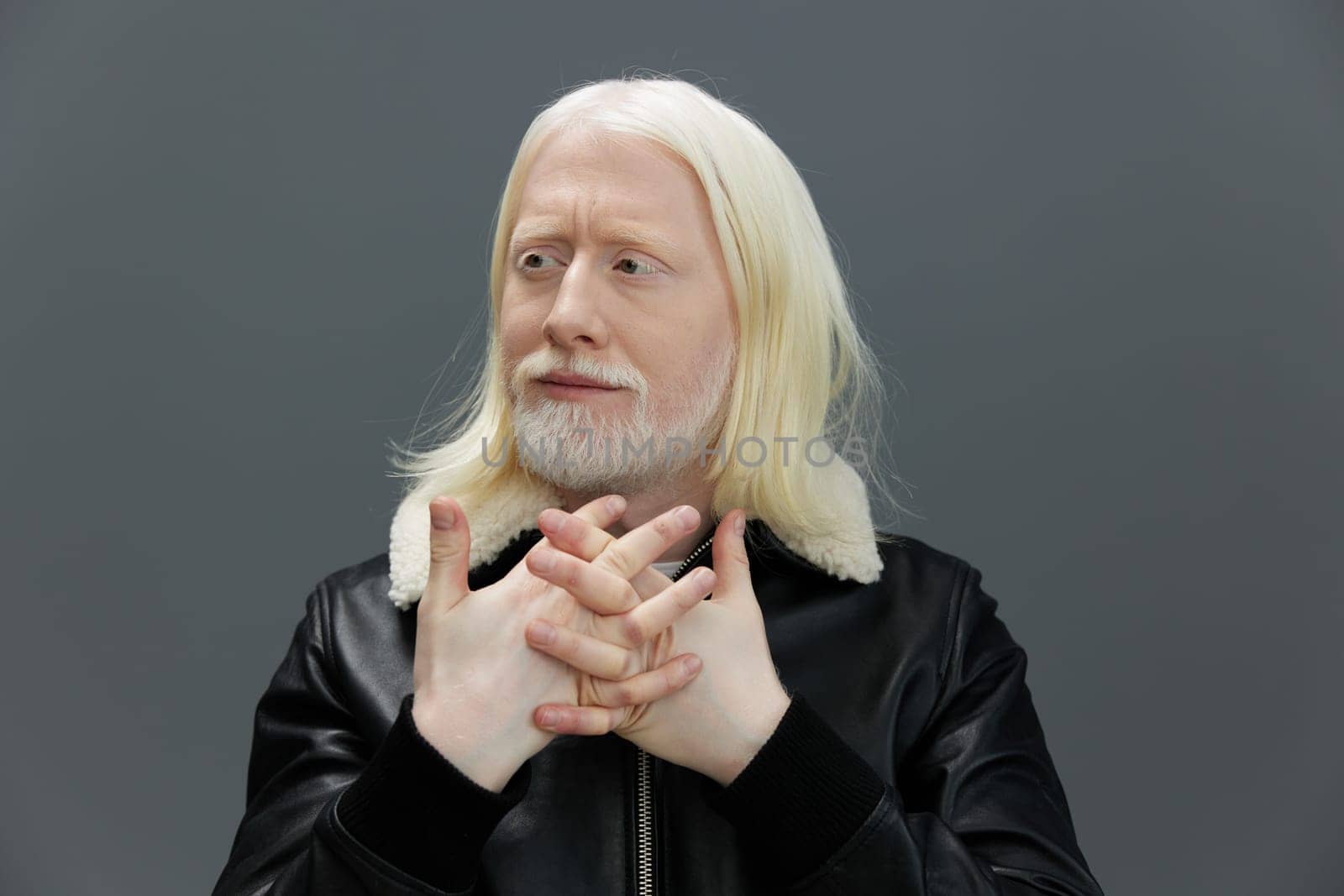 Pensive man with long blonde hair and a full beard in a black leather jacket posing against a plain gray background His expression reflects contemplation, making it suitable for themes of introspection and creativity