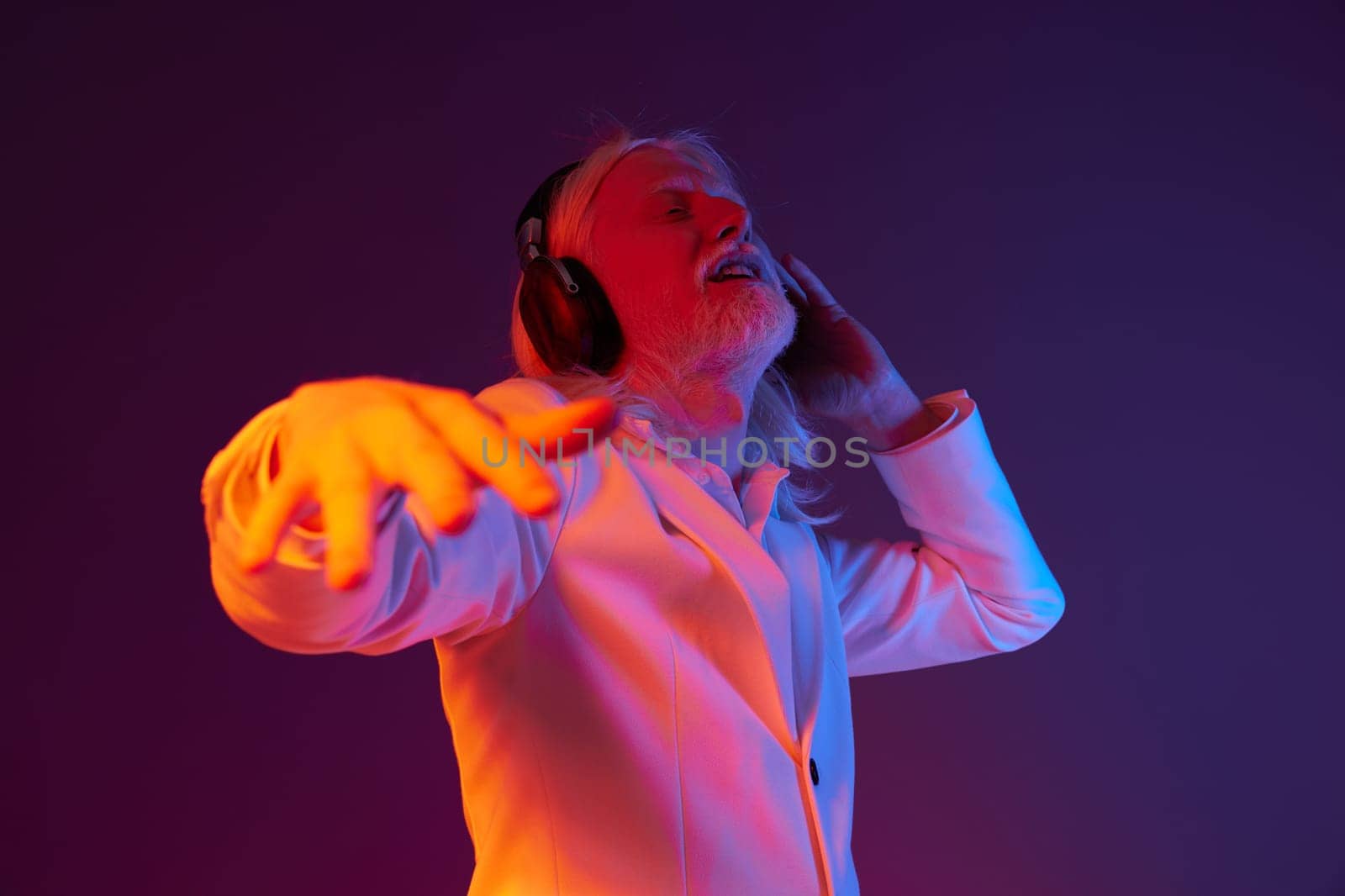 elderly man in a white jacket, immersed in music while wearing headphones, vibrant purple and orange background enhances the dynamic mood, showcasing joy and rhythm through expressive body language