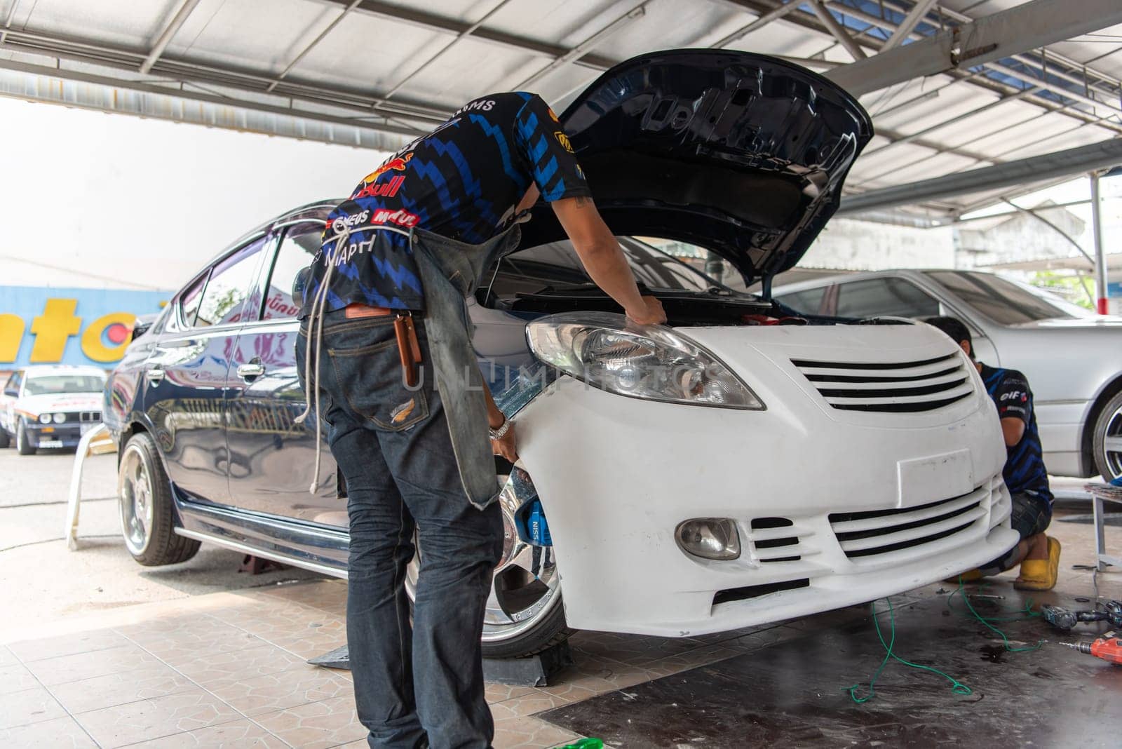 Bangkok, Thailand - April 4, 2024 : Unidentified denter or car mechanic serviceman check and fix body work and fiber bumper body part for fix and repair problem at car garage or repair shop