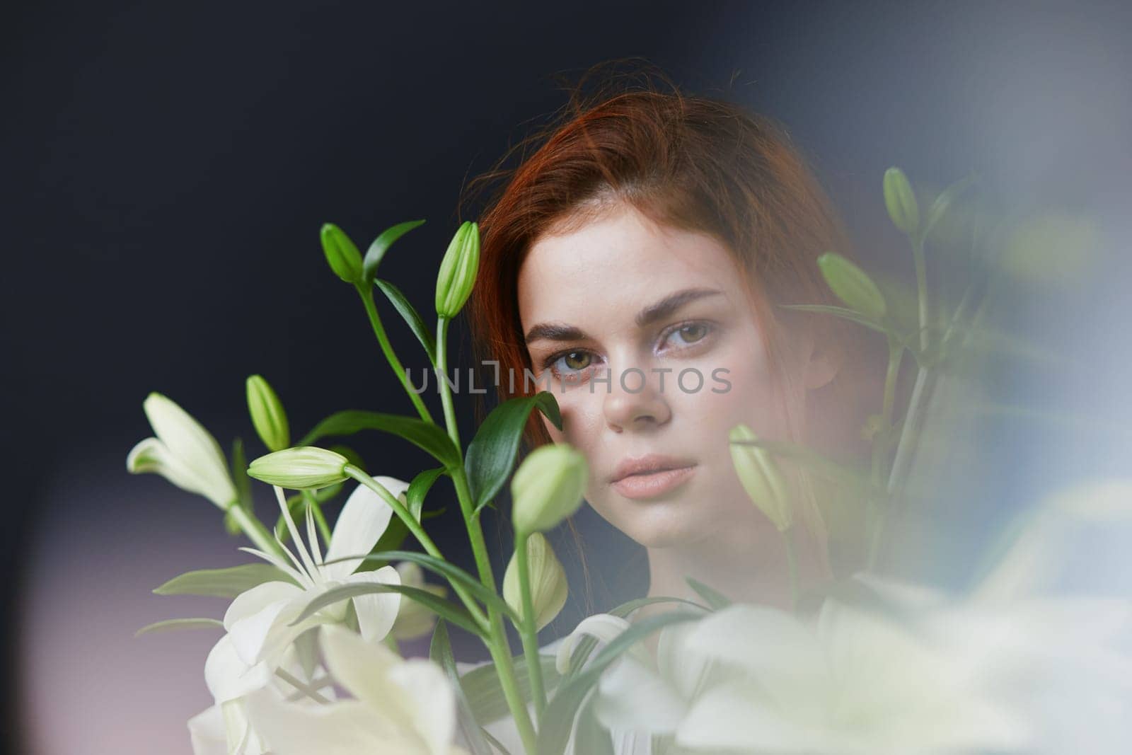 This image features a young woman with striking red hair, gently surrounded by white lilies Her calm and serene expression highlights themes of beauty, nature, and wellness Ideal for spring aesthet