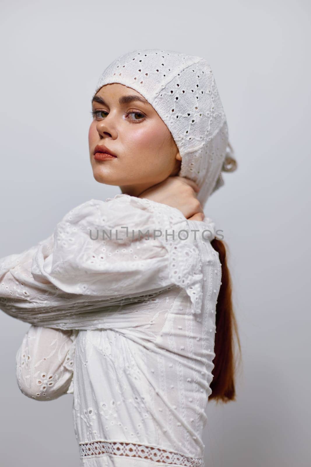 A confident young woman wearing a white embroidered dress and a matching headscarf showcases elegance and poise in a minimalist studio background with soft colors, perfect for fashion and portrait t
