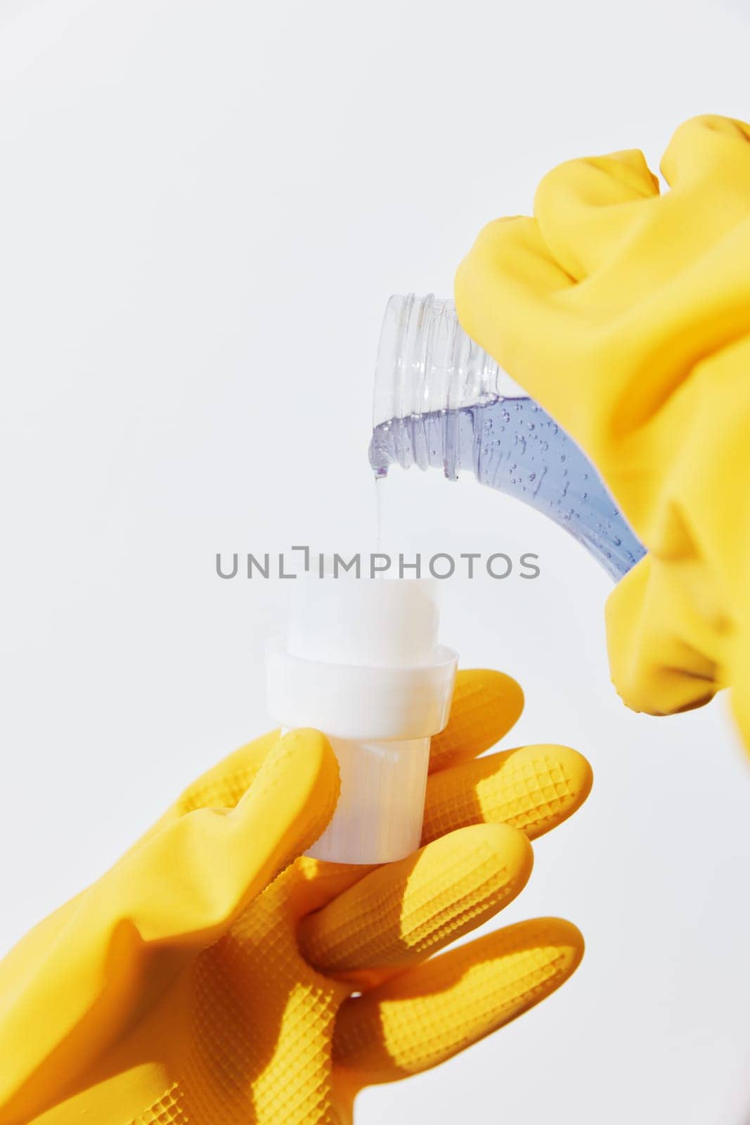 Two women wearing yellow rubber gloves are holding bottles of cleaning solution.