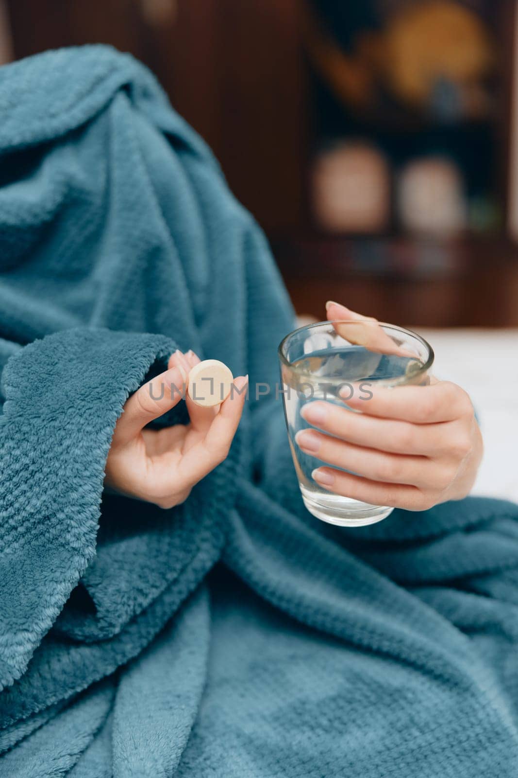 Woman in blue blanket with glass of water and pill bottle.