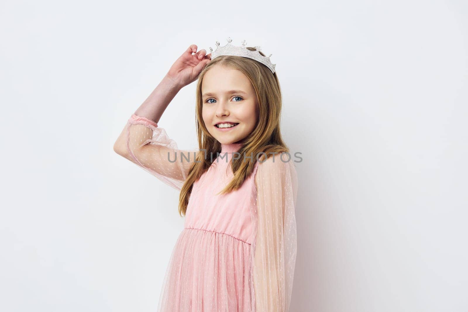 A cheerful young girl in a pink dress and crown, exuding happiness and innocence, poses against a light background, embodying joy and playful spirit in a child friendly concept