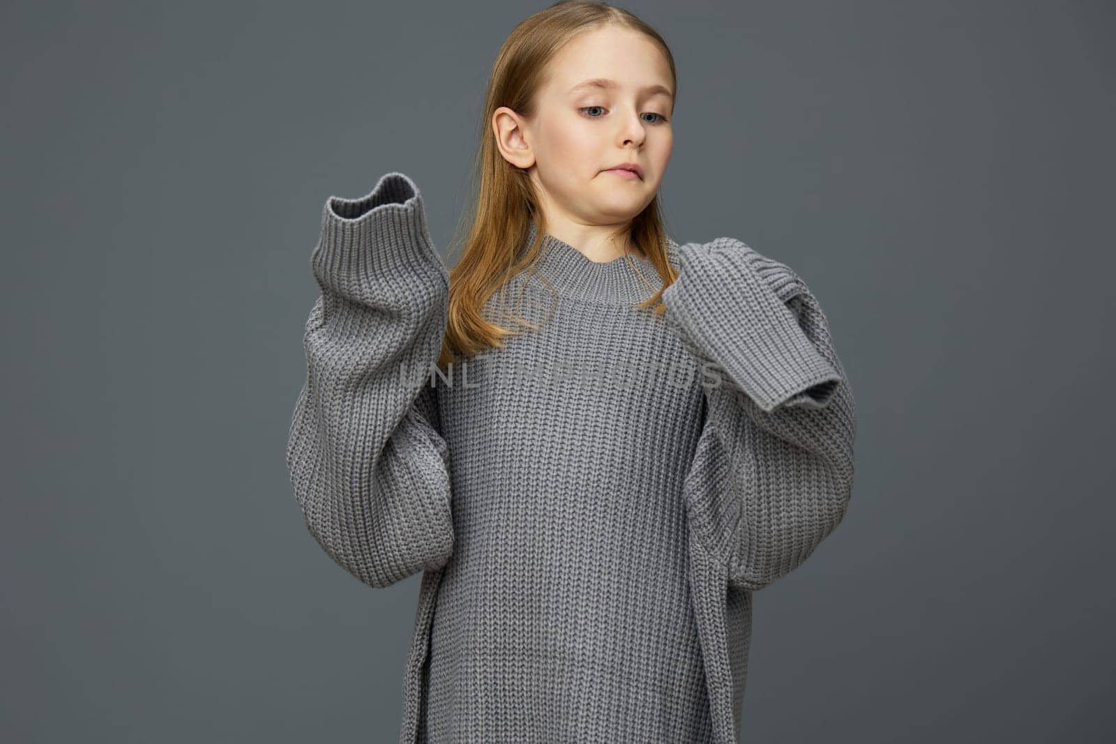 A young girl displaying a relaxed pose in an oversized gray sweater, radiating confidence and comfort The neutral gray background complements the fashion aesthetic, perfect for lifestyle and children s clothing themes