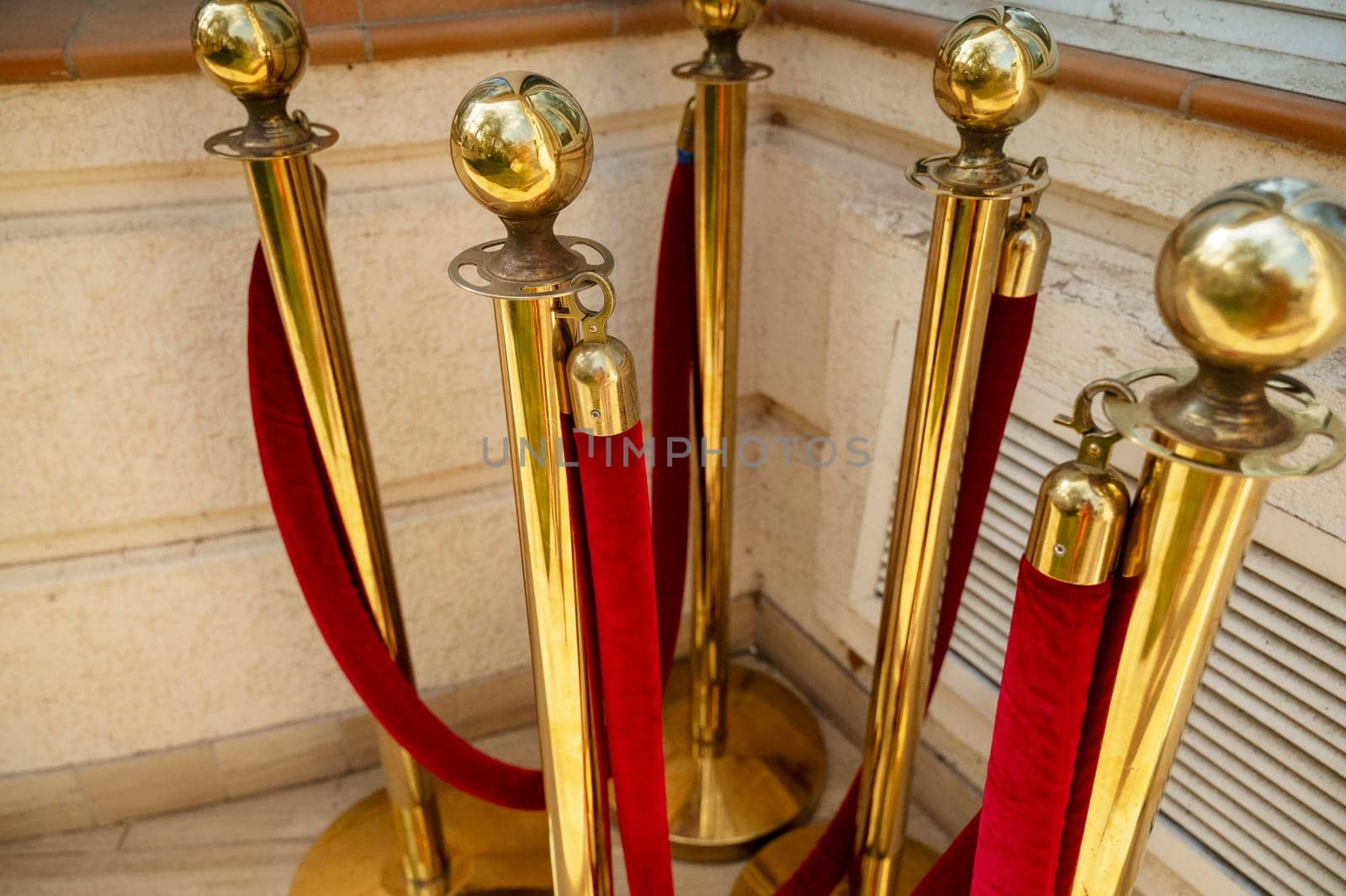 Gold colored metal stanchions with red velvet rope for crowd control. A group of red velvet ropes and gold poles on the street, waiting to be installed near the hotel building.