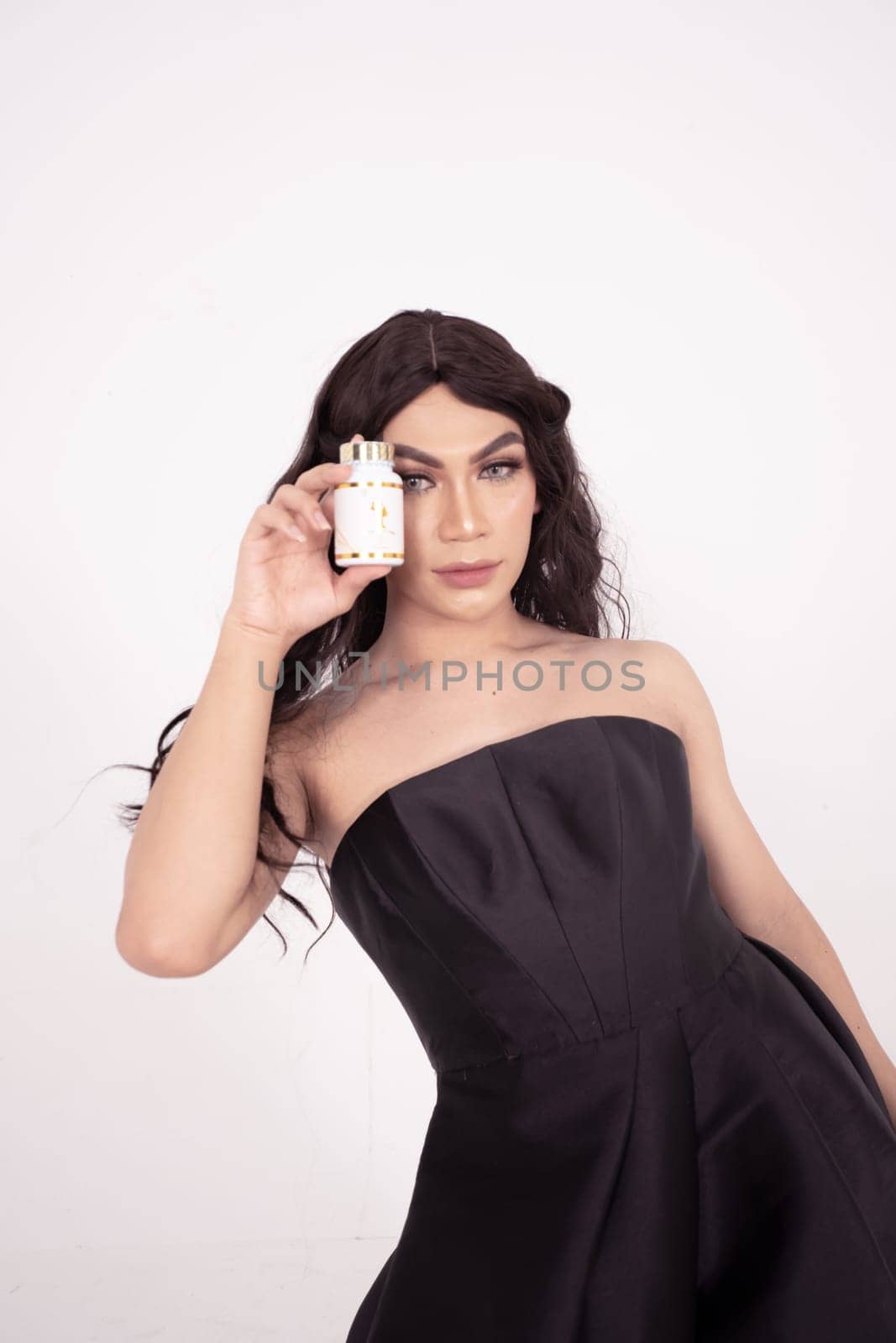 Asian woman poses with skincare in her hands while wearing a black wedding dress inside the studio