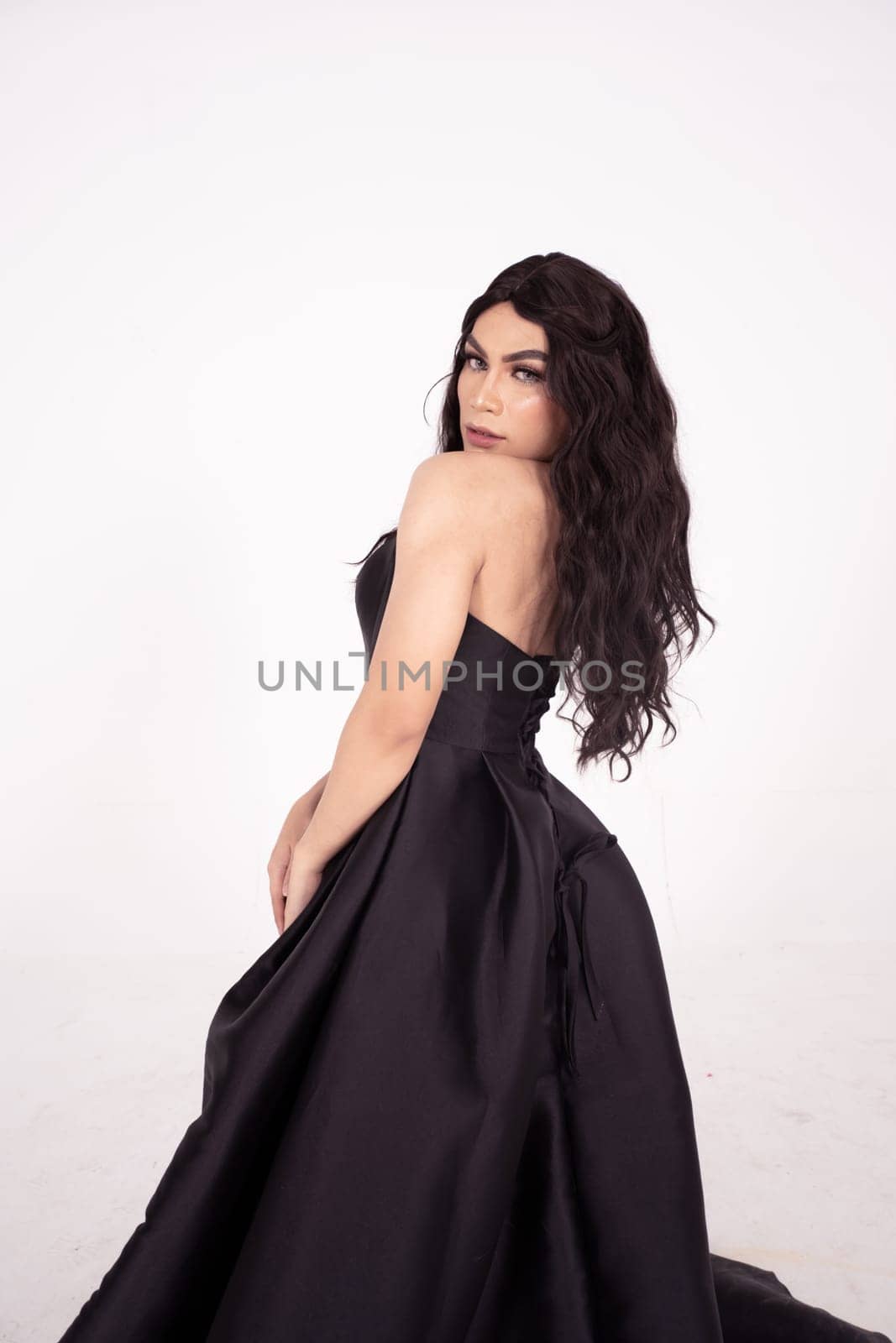 Beautiful woman with curly black hair while wearing a black dress inside the white room