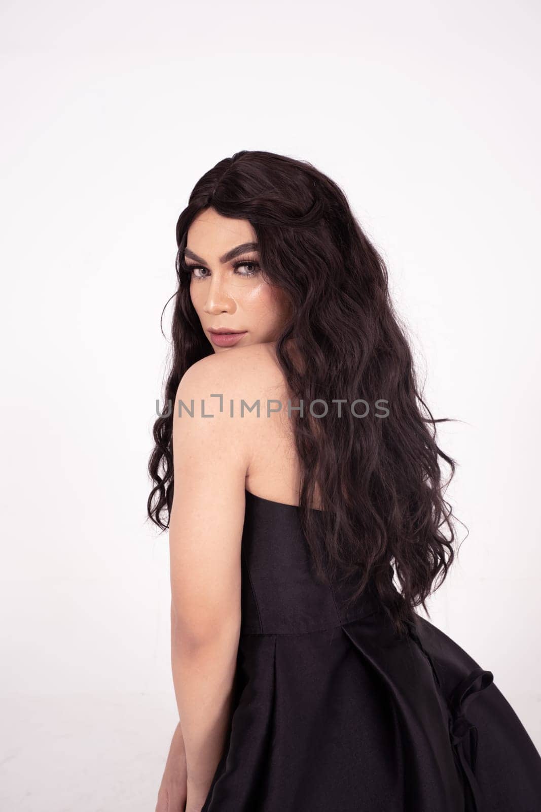 Beautiful woman with curly black hair while wearing a black dress inside the white room