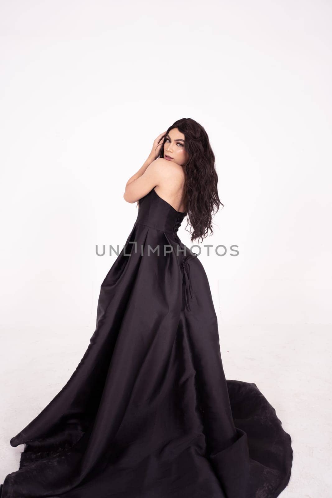 Beautiful woman with curly black hair while wearing a black dress inside the white room