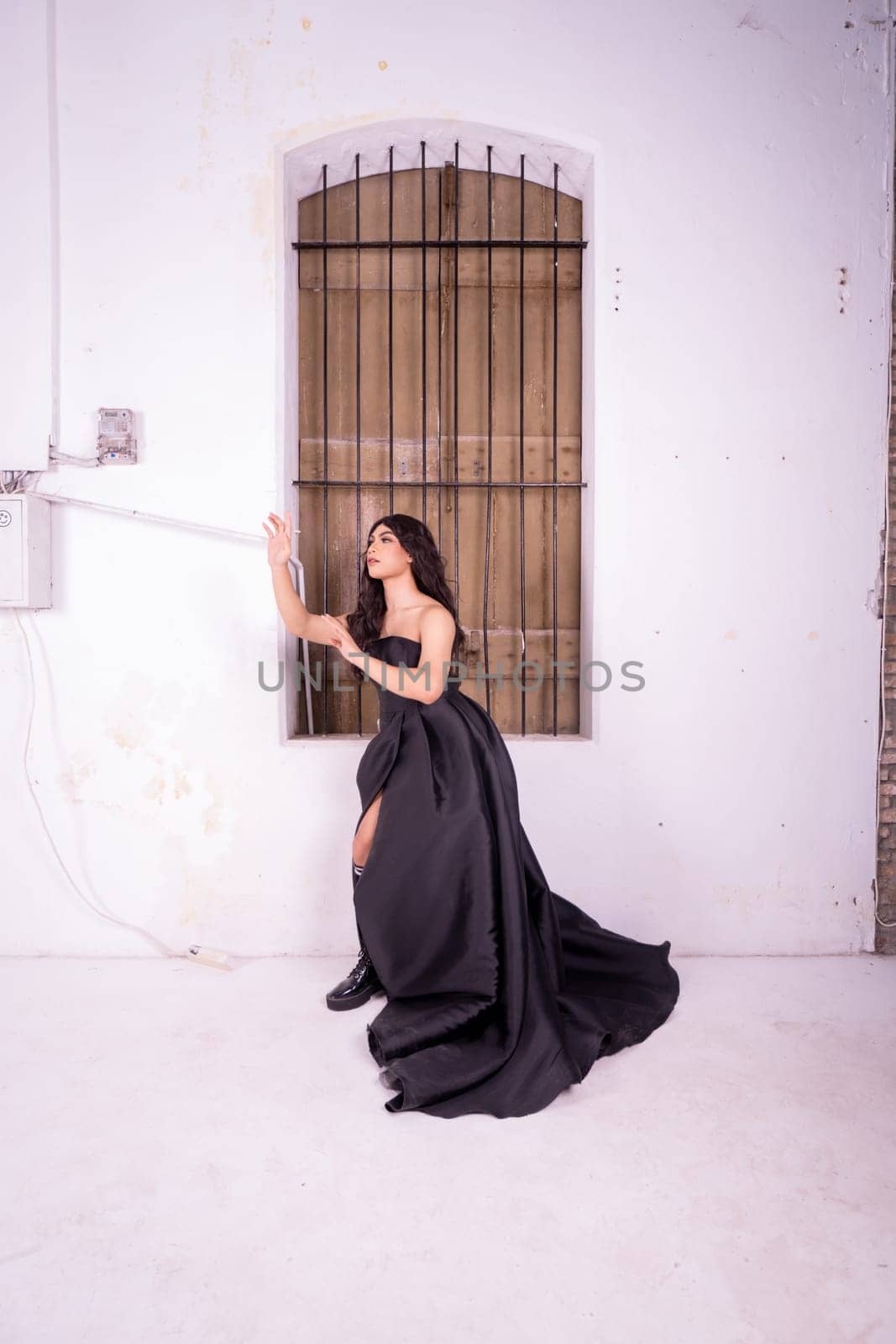 Sad Asian woman standing in front of the brown wooden window while wearing a black dress inside the studio