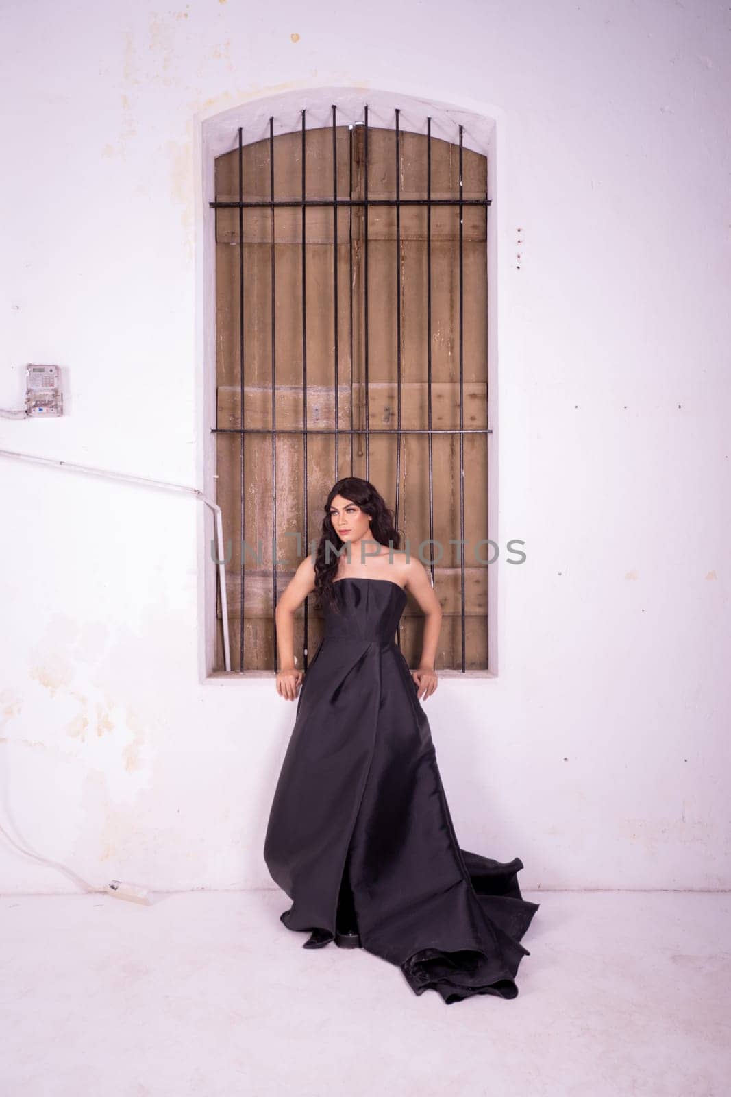 Elegance woman in a black dress standing in front of the rustic wooden window in a white studio