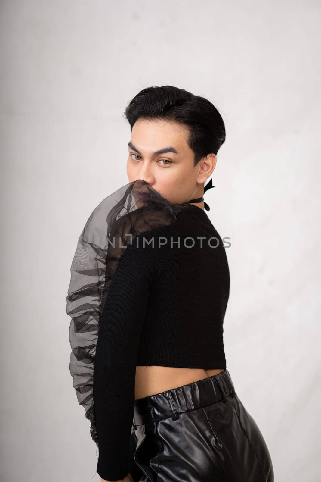 A transgender man poses in a black dress with an elegance face and black hair inside the white studio