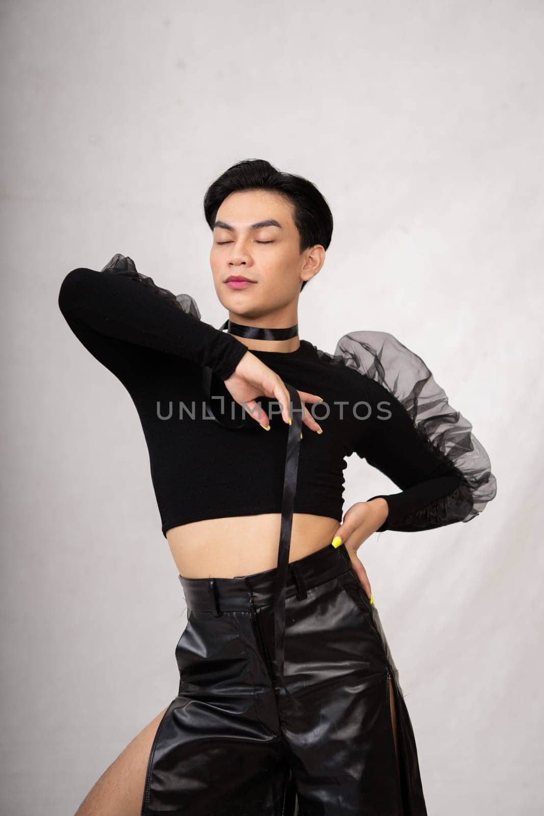 A transgender man poses in a black dress with an elegance face and black hair inside the white studio