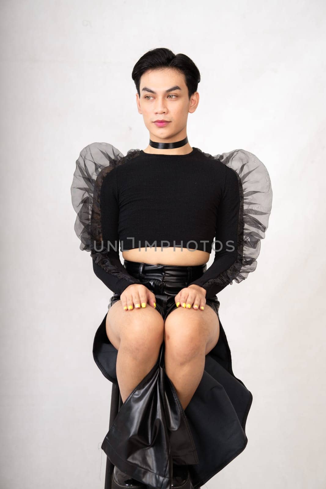 The beautiful man sitting on the chair while wearing a black costume with a pretty face inside the white studio