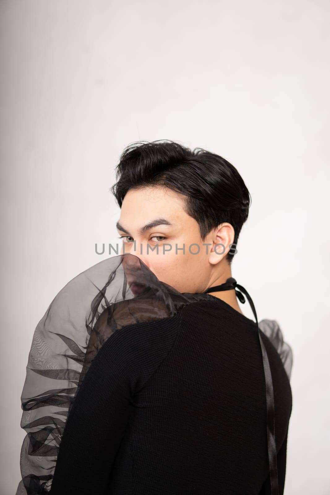 Asian man poses in a black costume while wearing makeup and black hair inside the studio