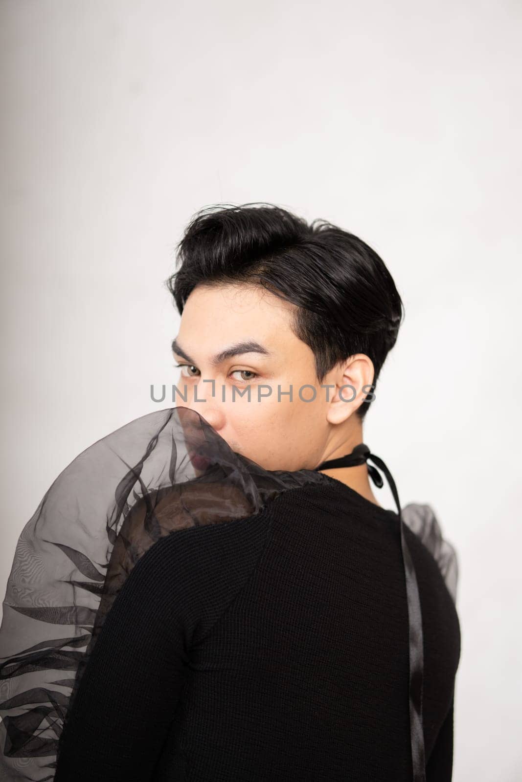 Asian man poses in a black costume while wearing makeup and black hair inside the studio