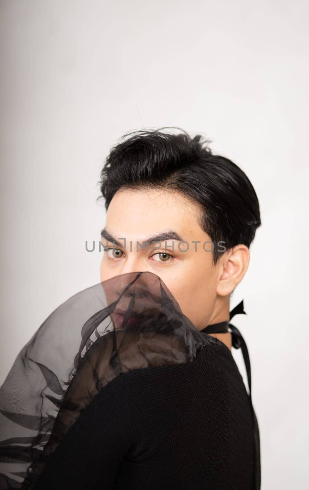 Asian man poses in a black costume while wearing makeup and black hair inside the studio