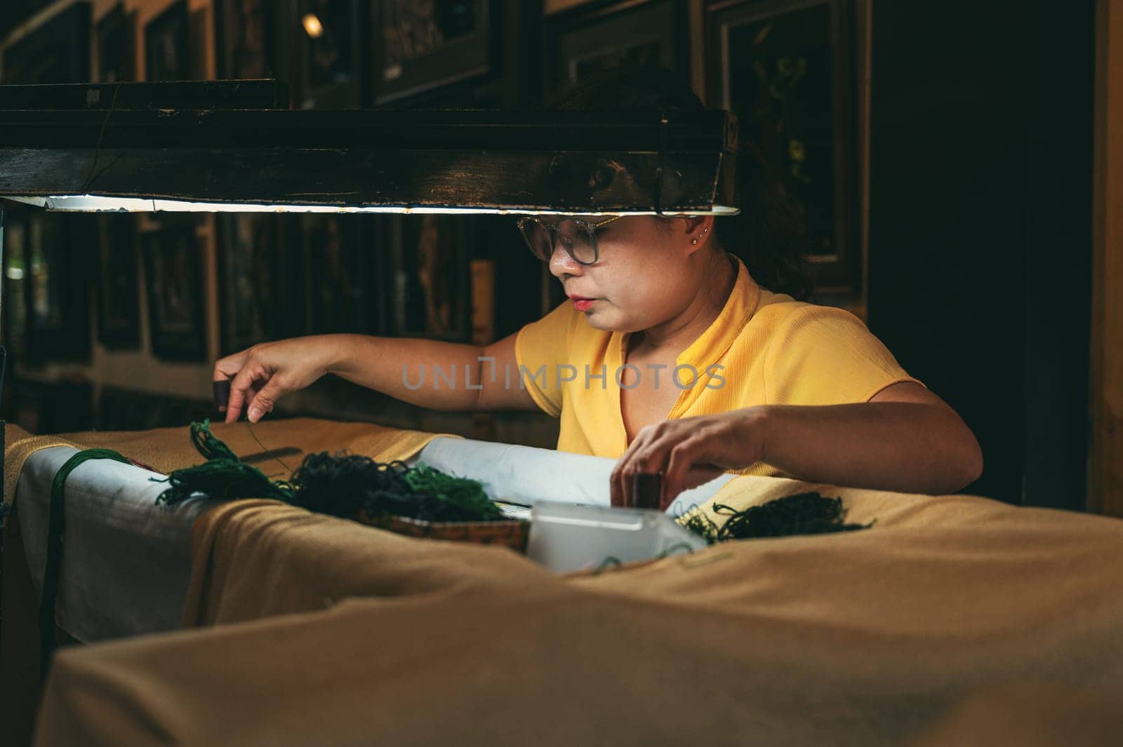 A Vietnamese female embroiderer embroiders a silk painting in a workshop in Hoi An city in Asia. Hoi An, Vietnam - December 1, 2024