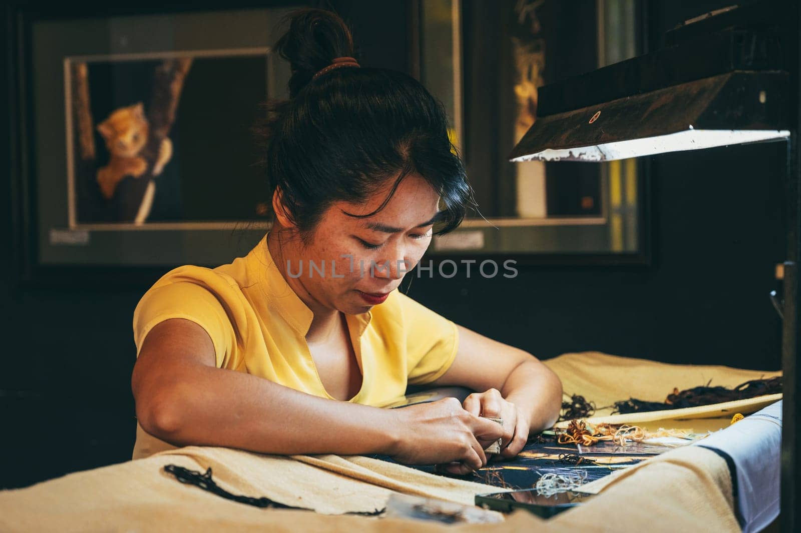 Vietnamese female embroiderer embroiders a silk painting in a workshop in the old town in Hoi An city in Vietnam in Asia. Hoi An, Vietnam - December 1, 2024