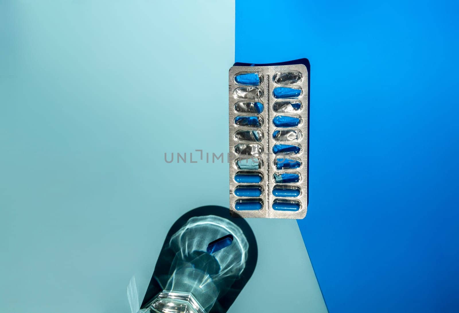 Medicine in blue capsules on a blue background. The background is light and dark blue. A glass of water and capsules in a blister. Space for text, top view. The concept of a medical pharmacy