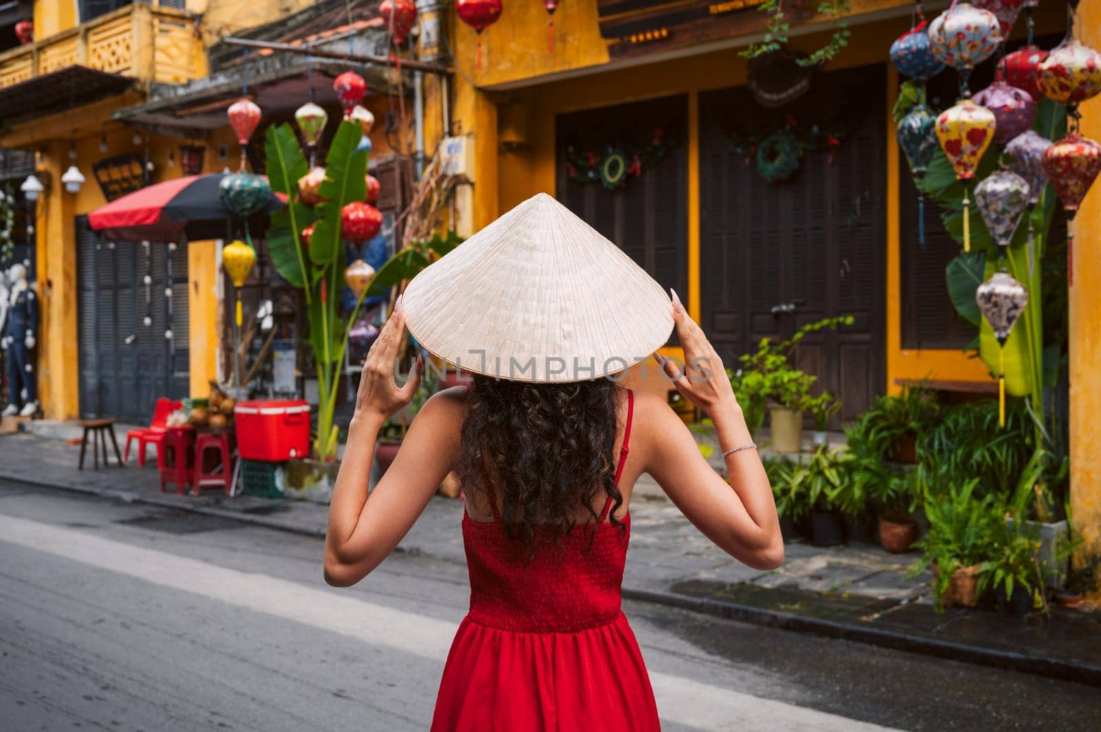 back of asian woman tourist in a traditional Vietnamese hat and red dress on the street in Hoi An city in Vietnam in Asia