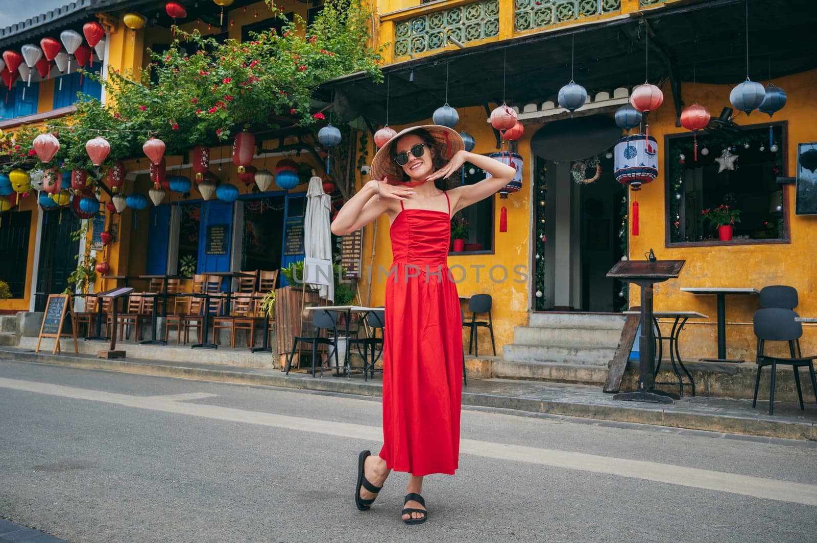 happy young female tourist traveler in traditional Vietnamese hat and red dress on street in Hoi An city in Vietnam in Asia
