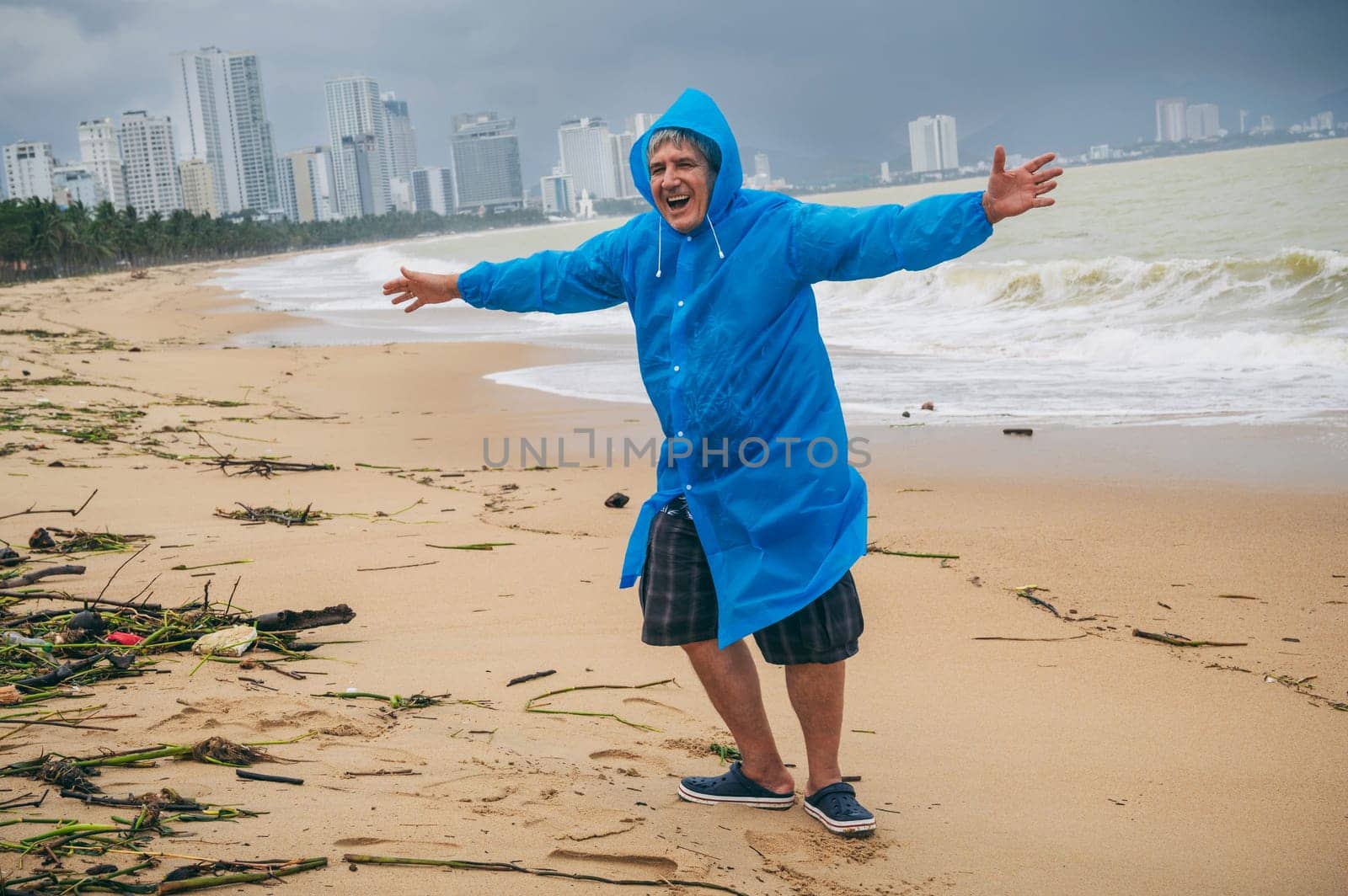 happy man tourist in a raincoat on a dirty beach by the sea after a storm in cloudy weather. The concept of the rainy and monsoon season