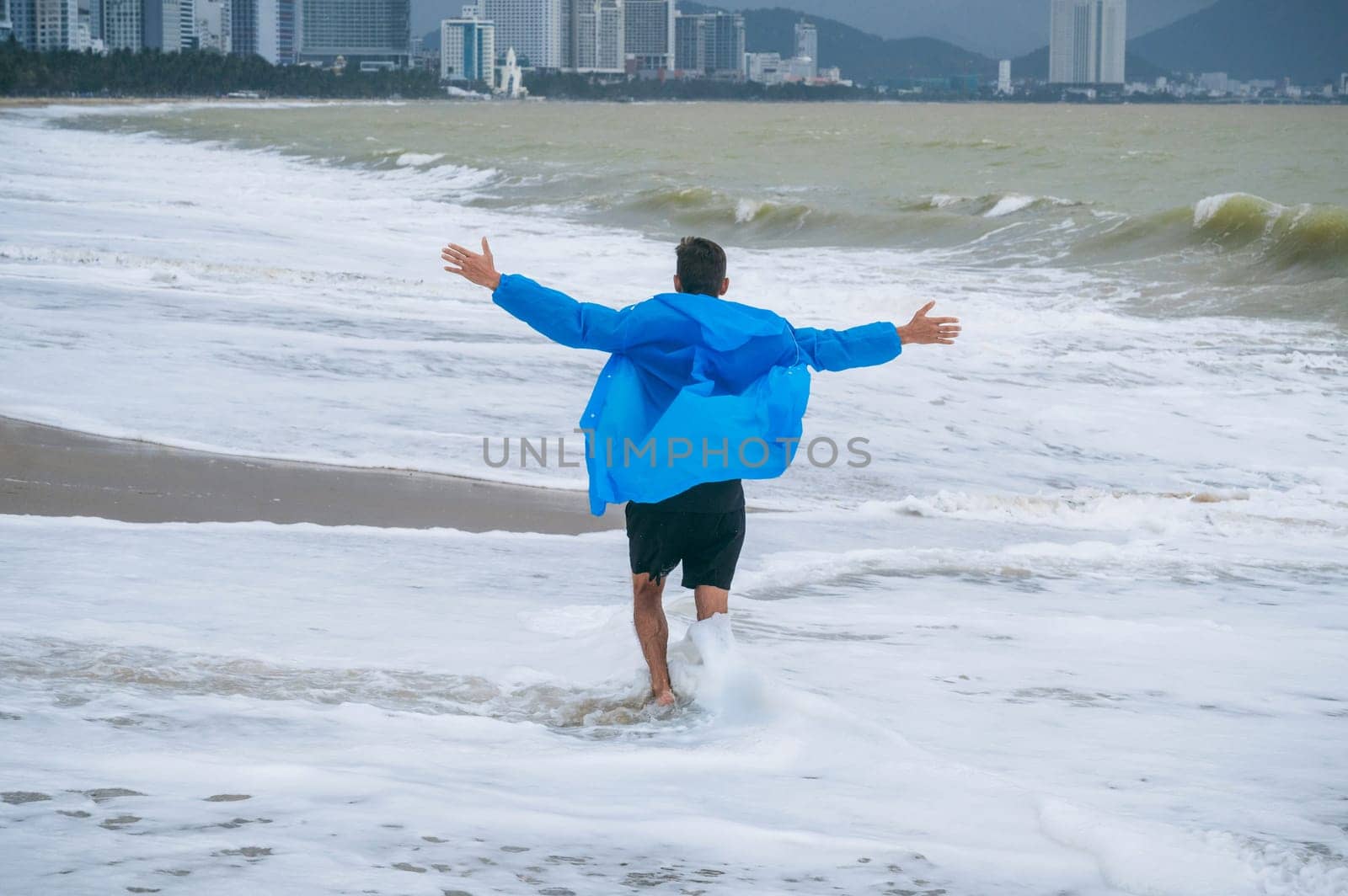 back of a man in a raincoat running along the beach by the sea with waves in cloudy weather with rain. The concept of the rainy and monsoon season