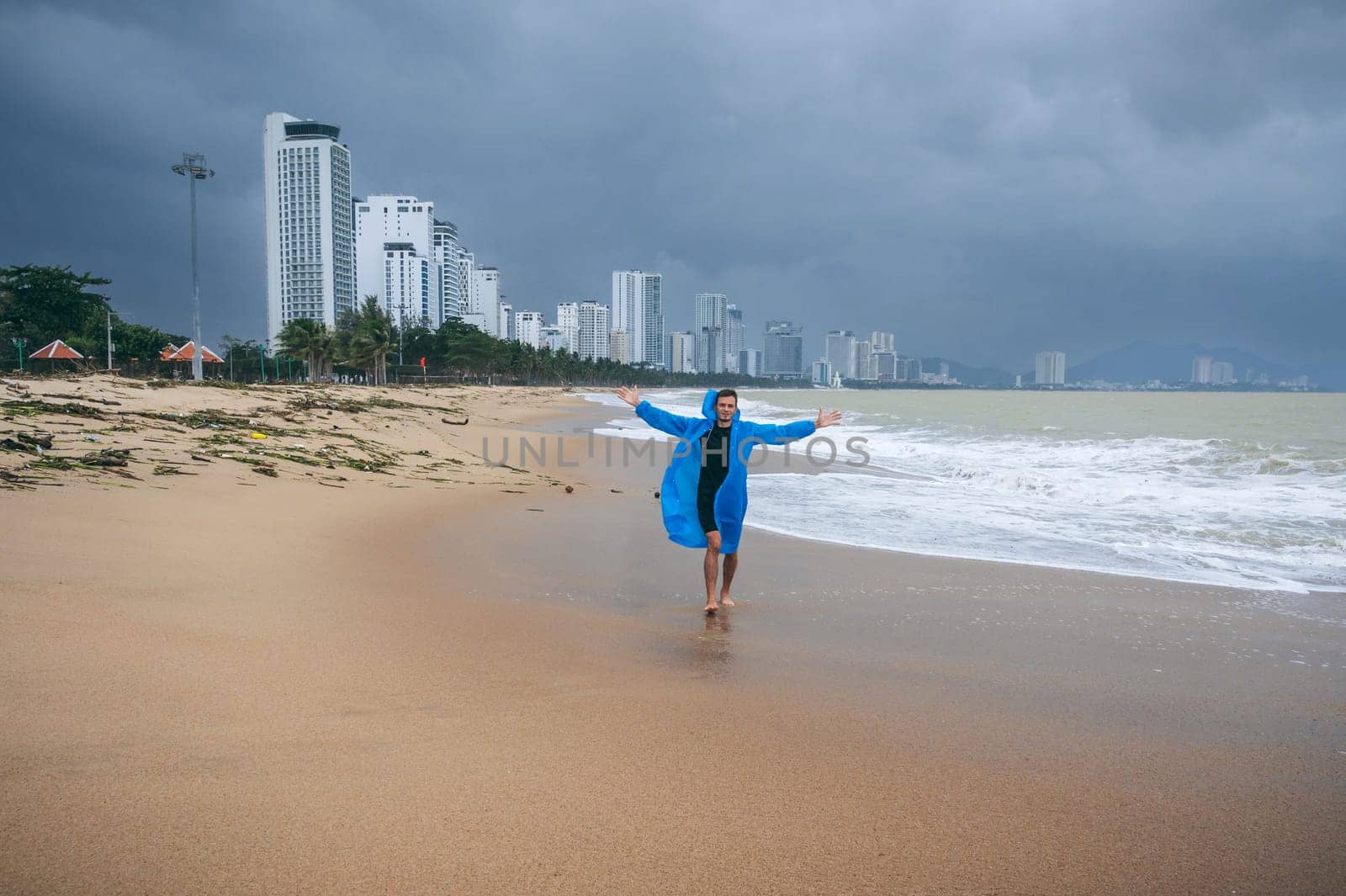 male in a raincoat on beach by sea with waves in cloudy weather with rain. Concept of rainy and monsoon season in Nha Trang in Vietnam