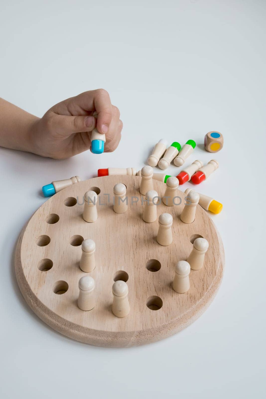 Child playing with wooden board game featuring colorful pegs and die.