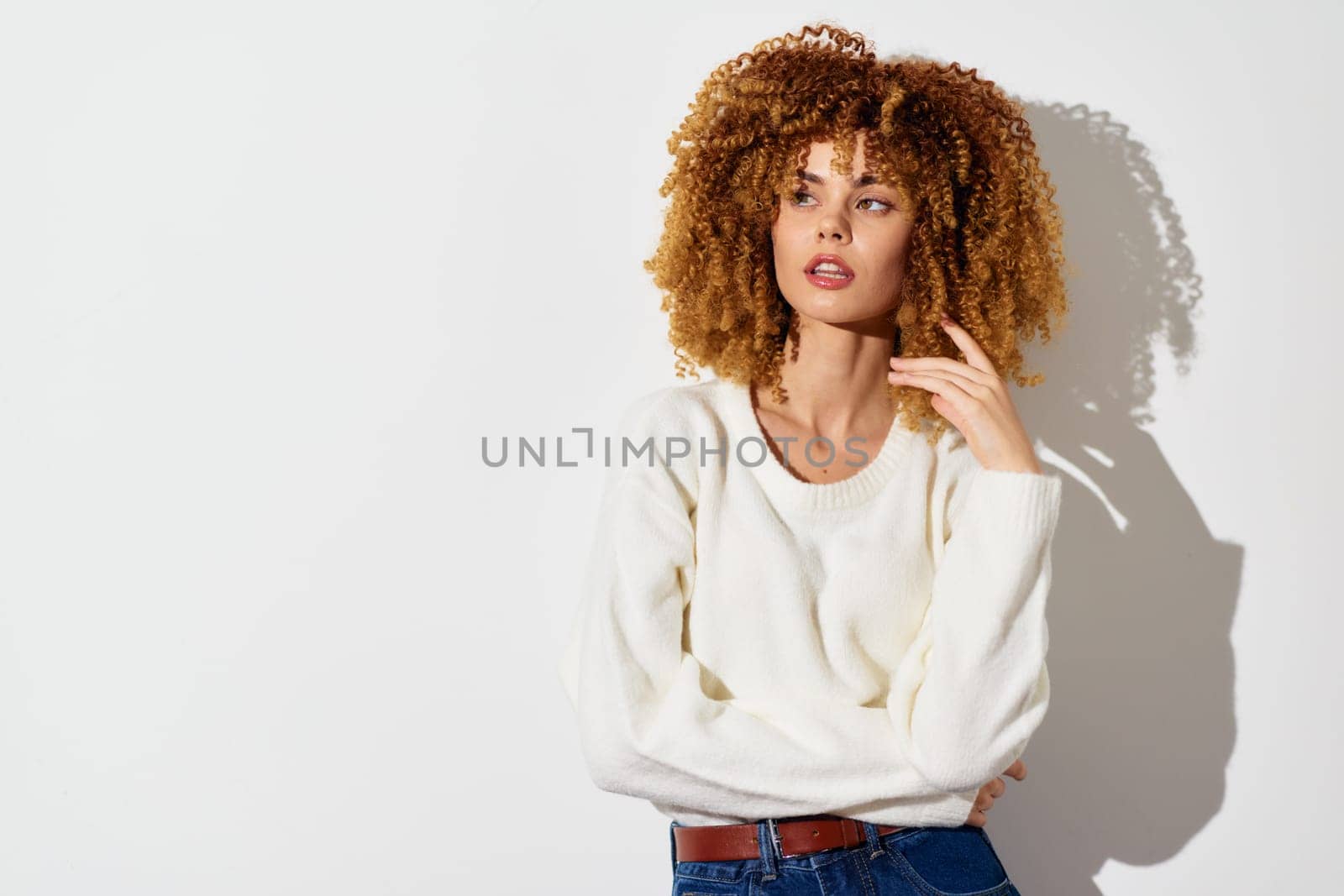 This image features a young woman with beautiful curly hair, wearing a white sweater, posed against a light background The relaxed ambiance highlights contemporary fashion