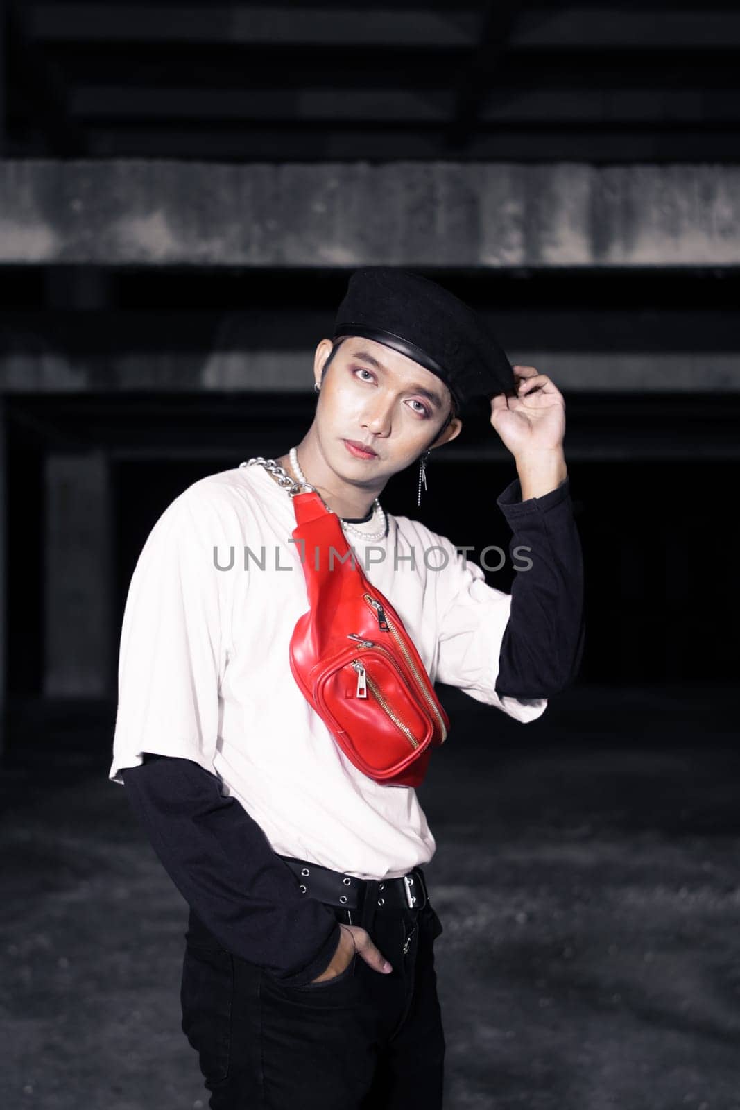 an Asian man in a white shirt wearing a red bag and a black hat in an old building at night